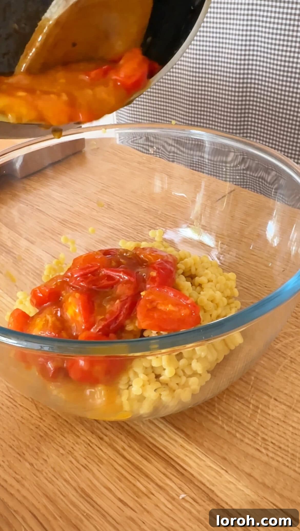 Pouring the tomato dressing into a bowl of cooked giant couscous.
