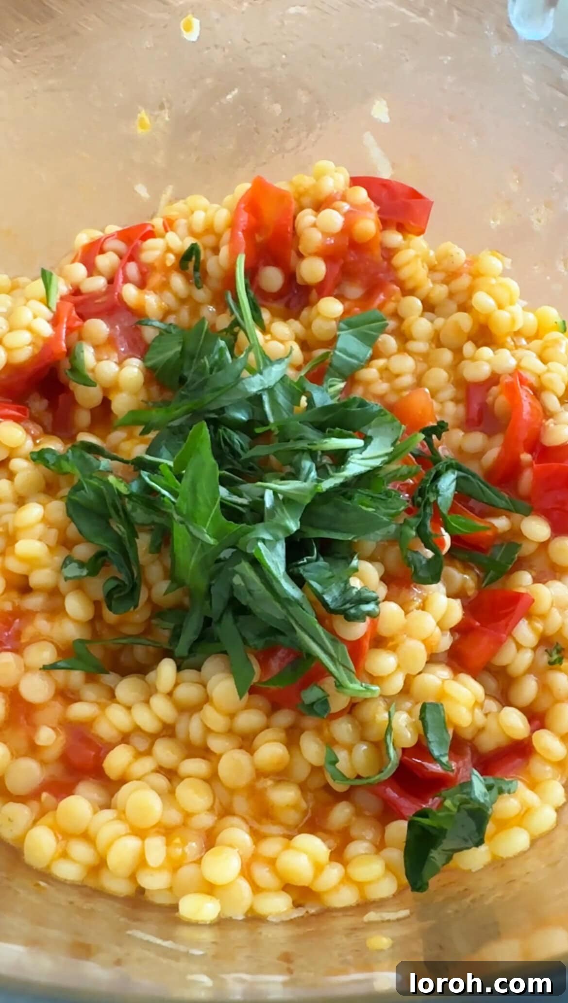 Mixing sliced basil into the giant couscous salad.