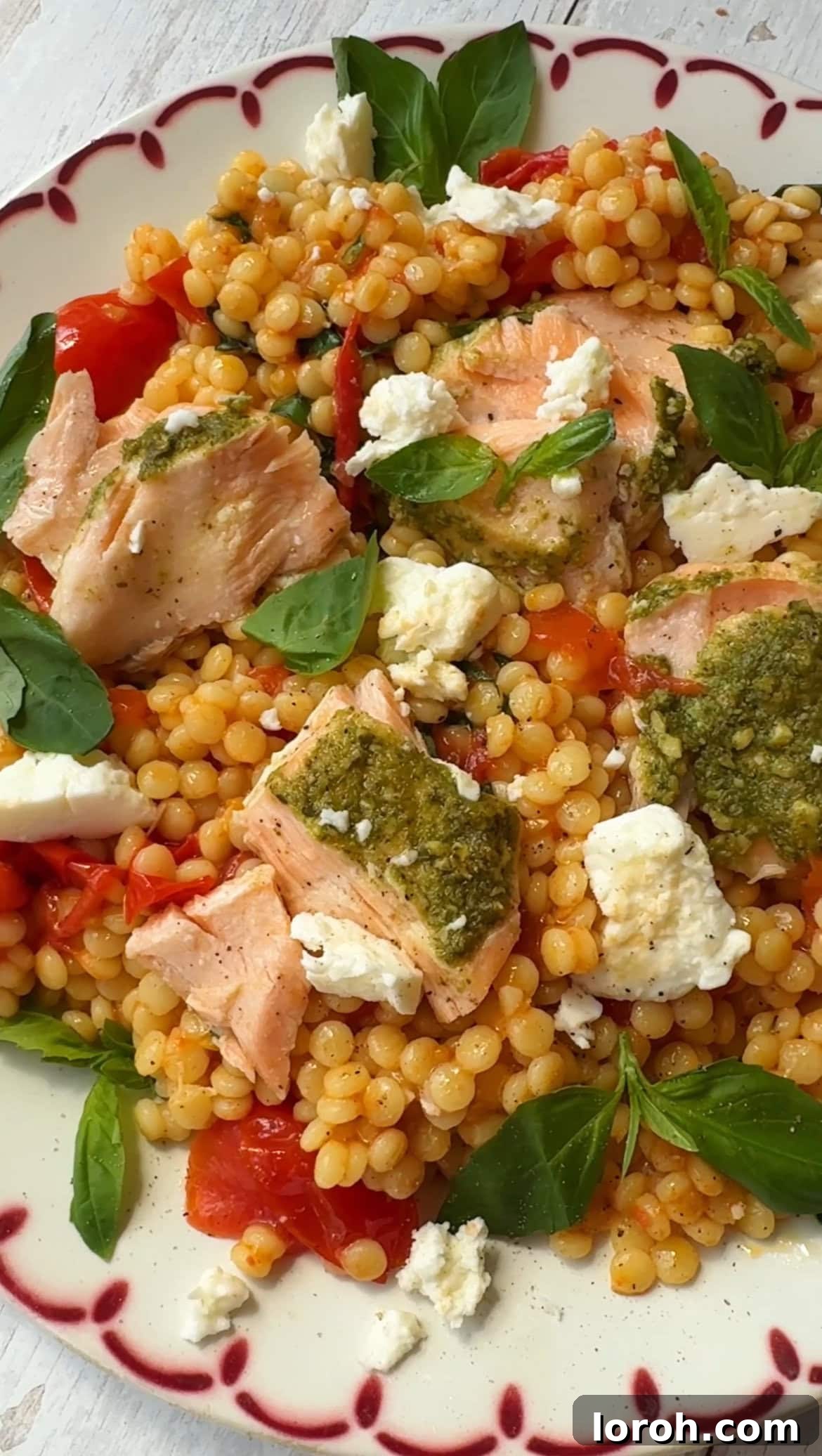 Two plates of Pesto Crusted Salmon with Roasted Tomato Giant Couscous Salad, garnished and ready to serve.