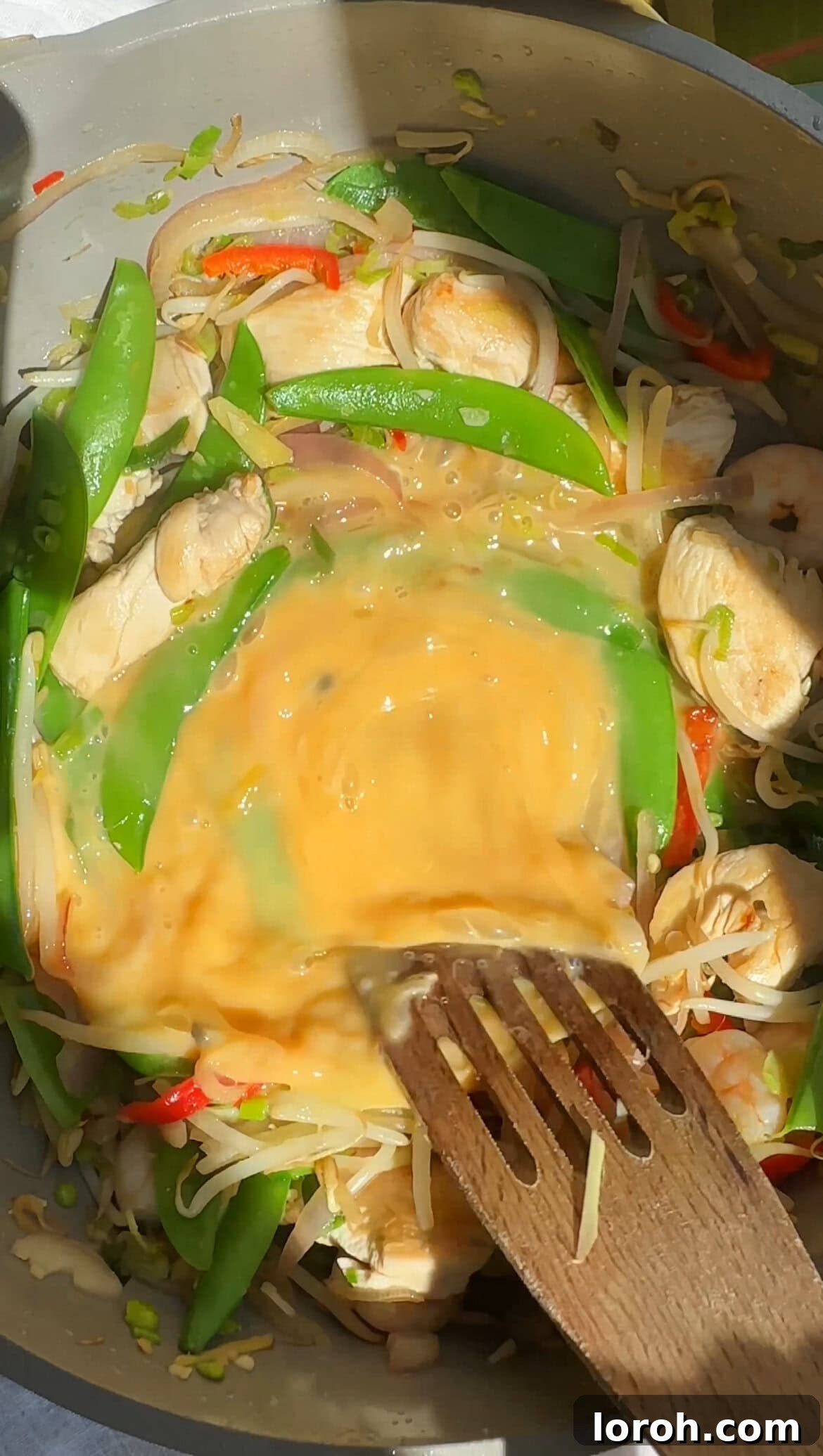 Adding beaten eggs to the stir-frying Pad Thai ingredients.