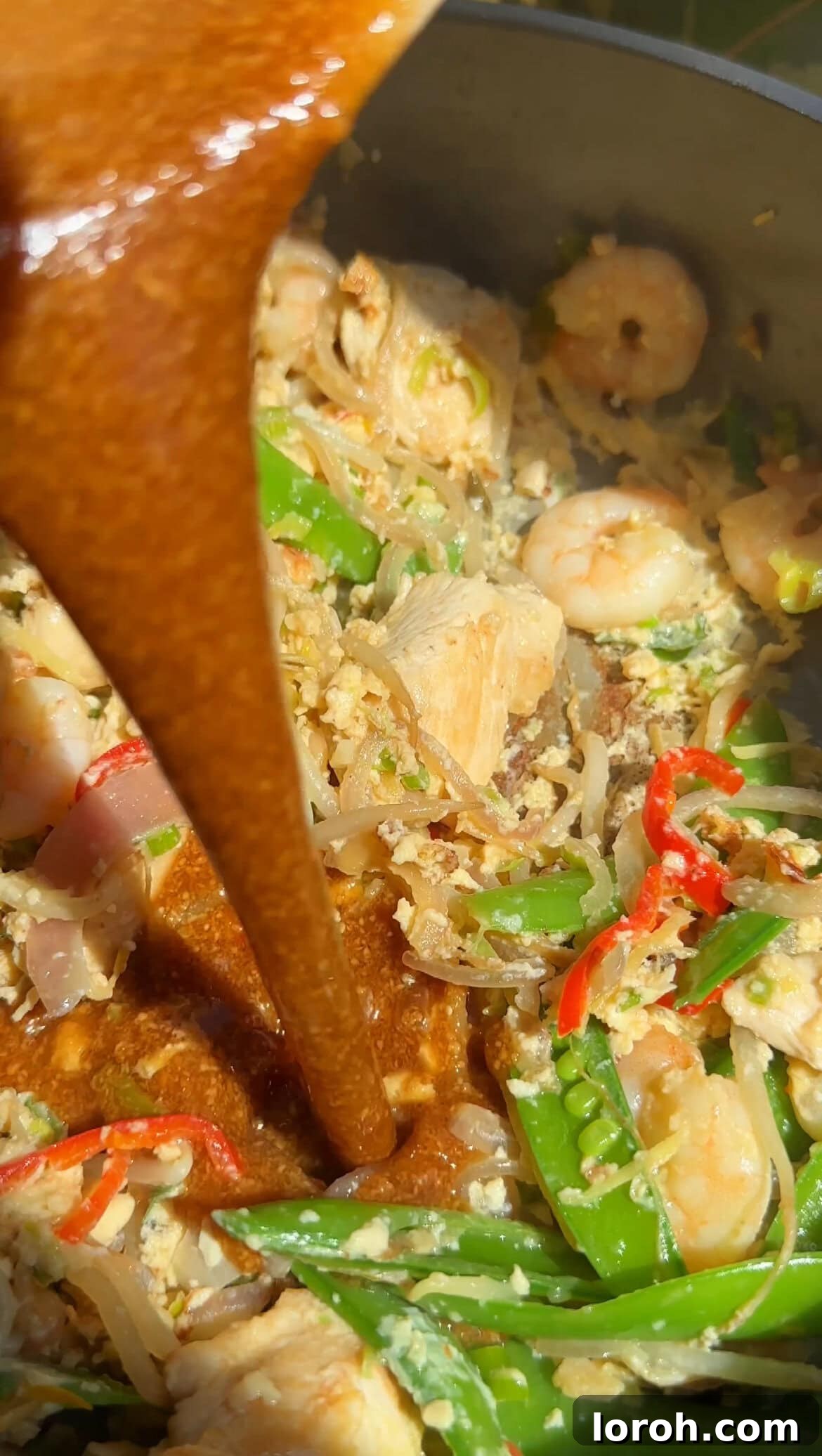 Pouring the Pad Thai sauce over the stir-fried ingredients in a wok.