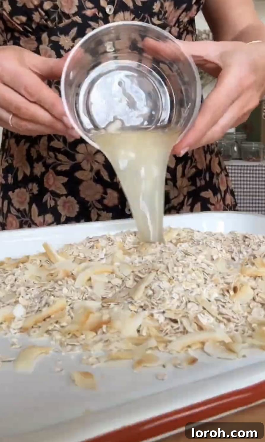 Pouring melted coconut oil over oats and coconut on a baking sheet.