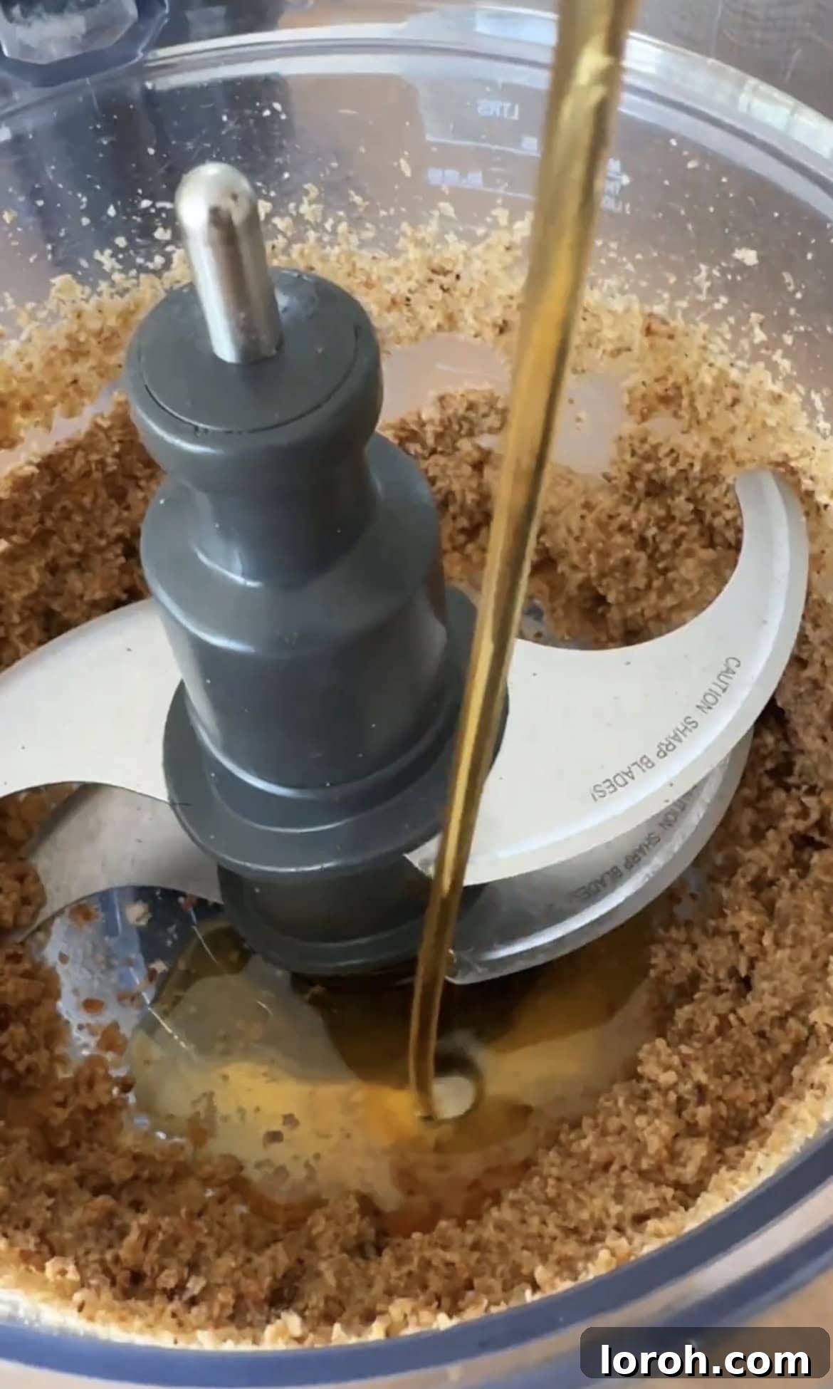 Adding maple syrup to toasted granola in a food processor.