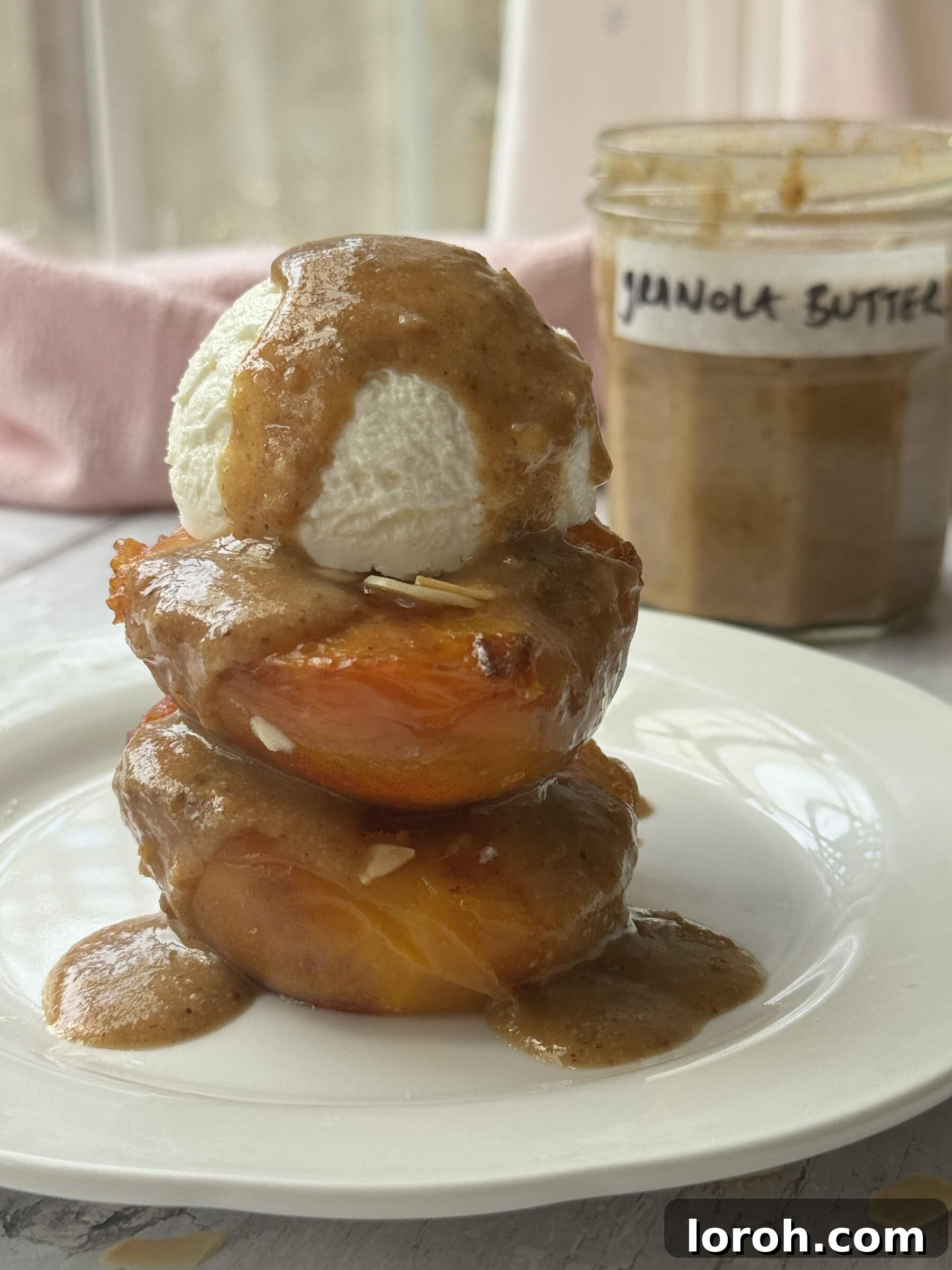 Creamy granola butter drizzled over roasted peaches on a white plate, ready to be served.