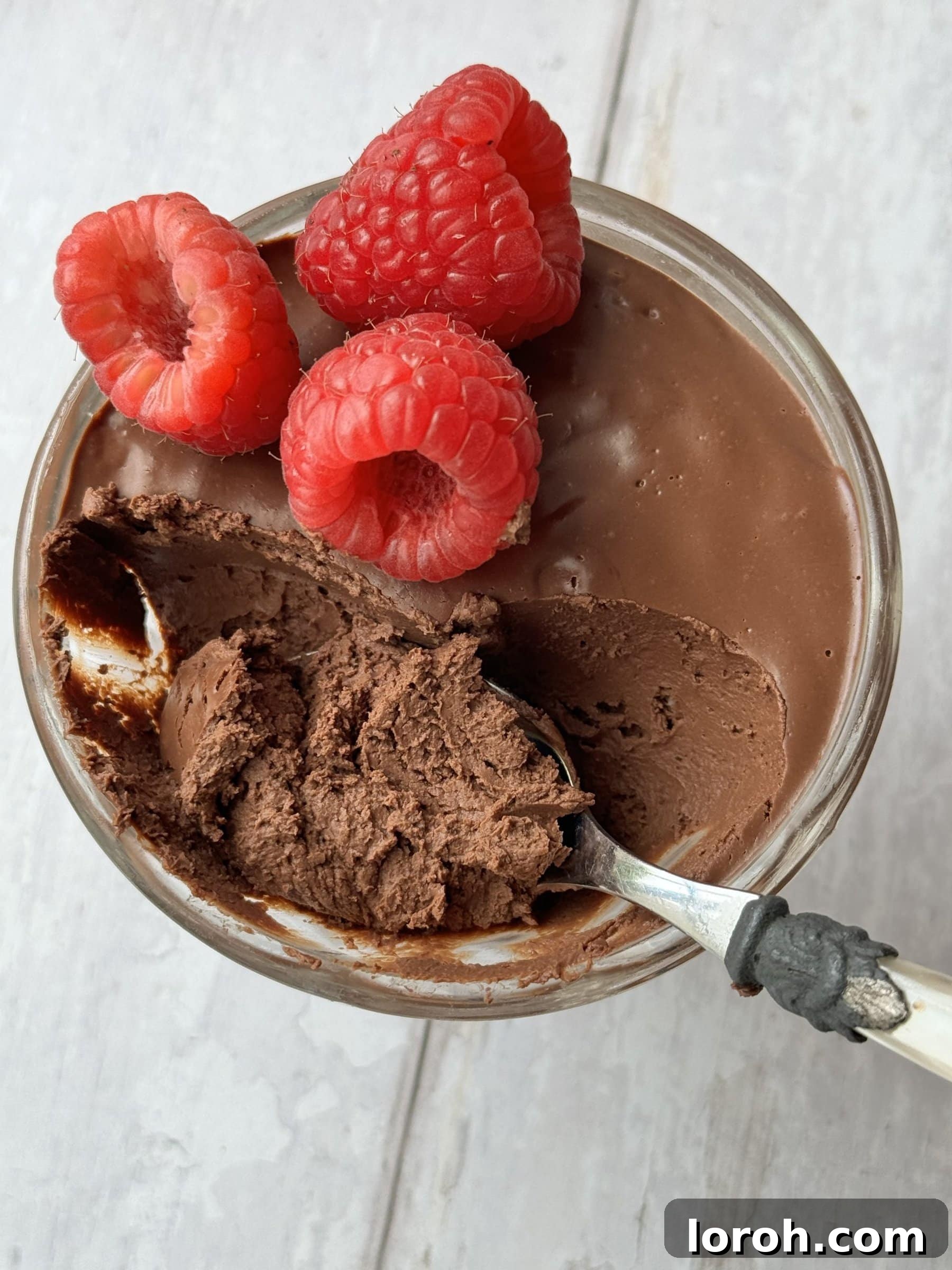 Velvety Protein Chocolate Mousse 2 chocolate protein mousse in a glass coupe with raspberries on top and a spoon