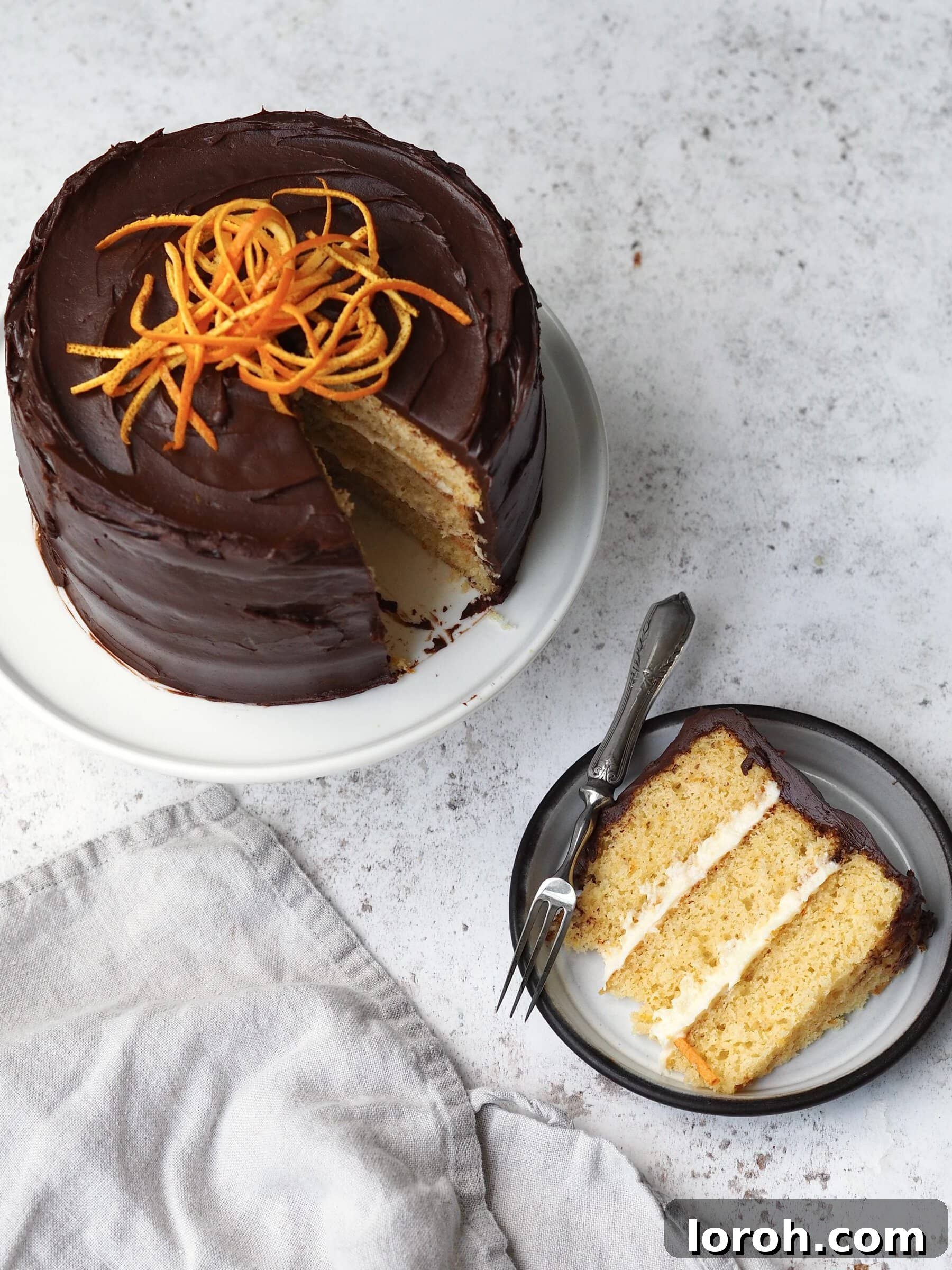 A slice of Jaffa Cake Cake removed from a whole cake on a black plate, showcasing the layers of orange sponge, marmalade buttercream, and chocolate ganache.