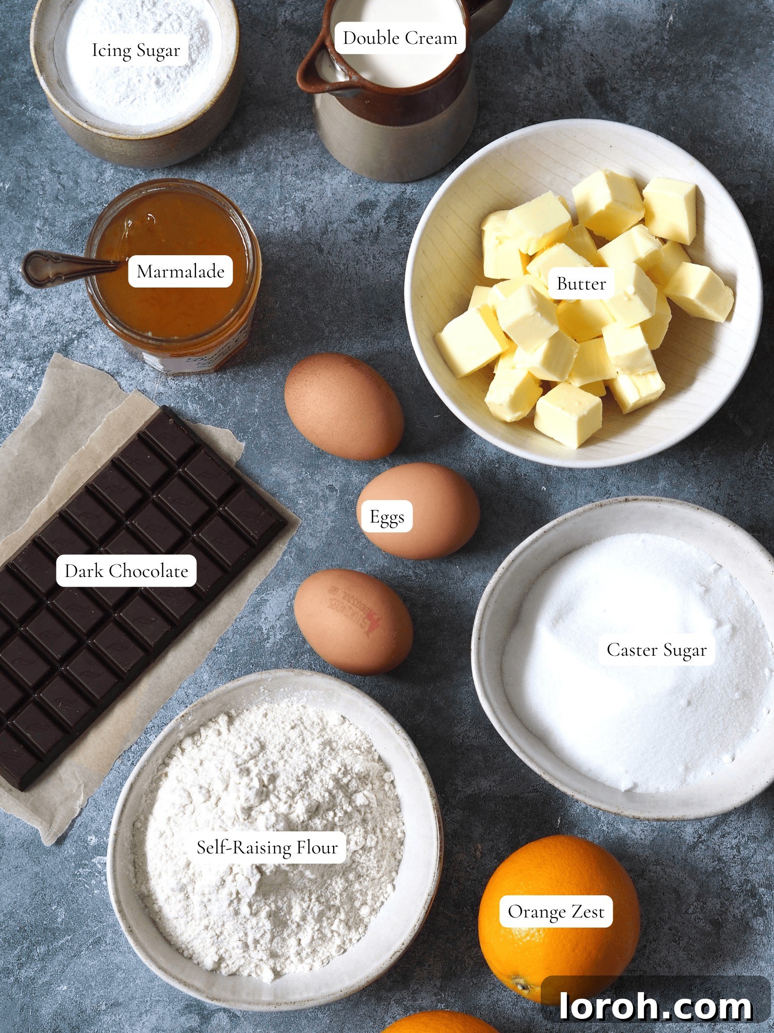 A flat lay of ingredients for Jaffa Cake Cake, including butter, eggs, flour, sugar, oranges, marmalade, chocolate, and cream.