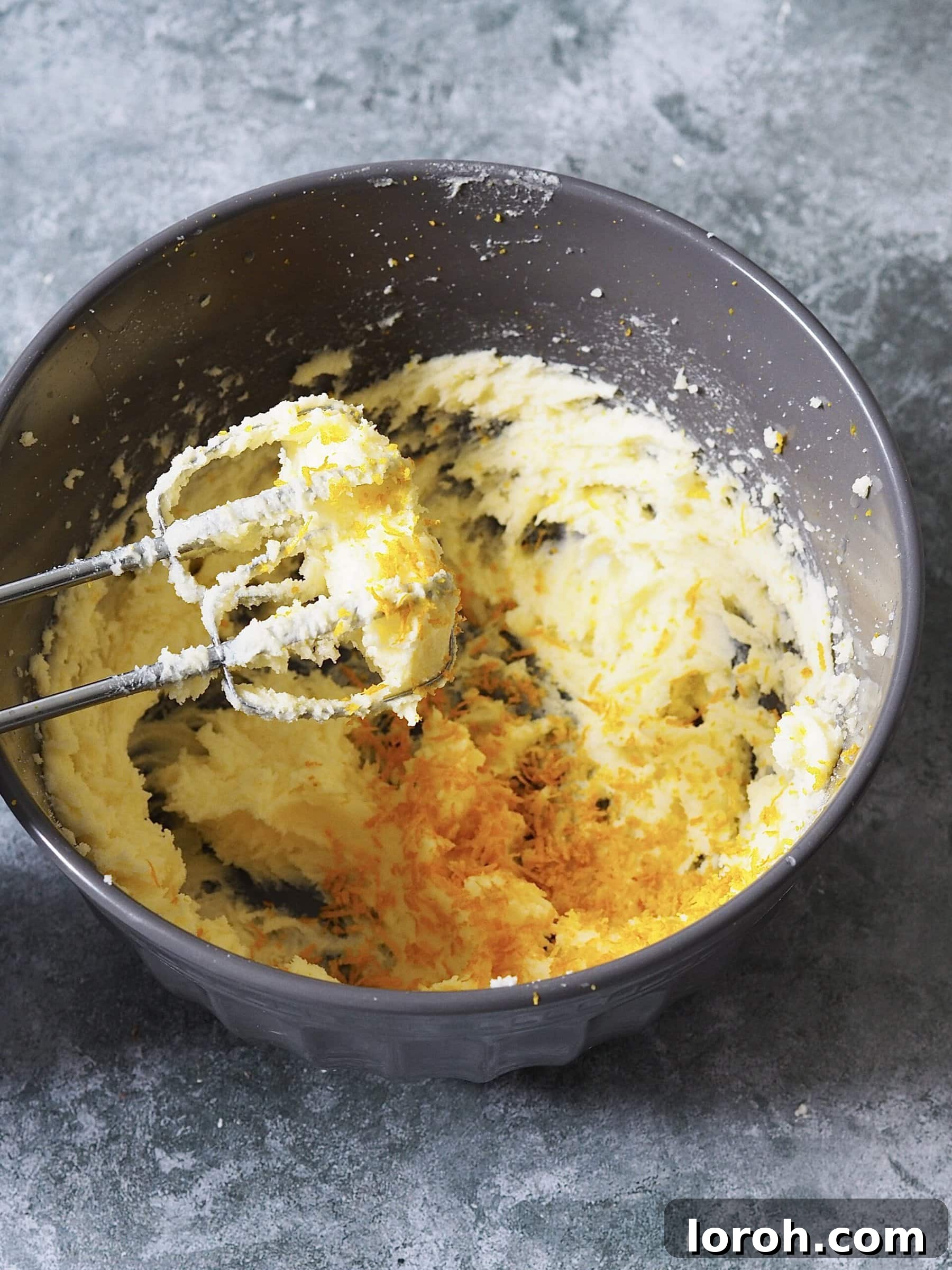 Mixing butter, sugar, and orange zest with an electric whisk in a bowl.