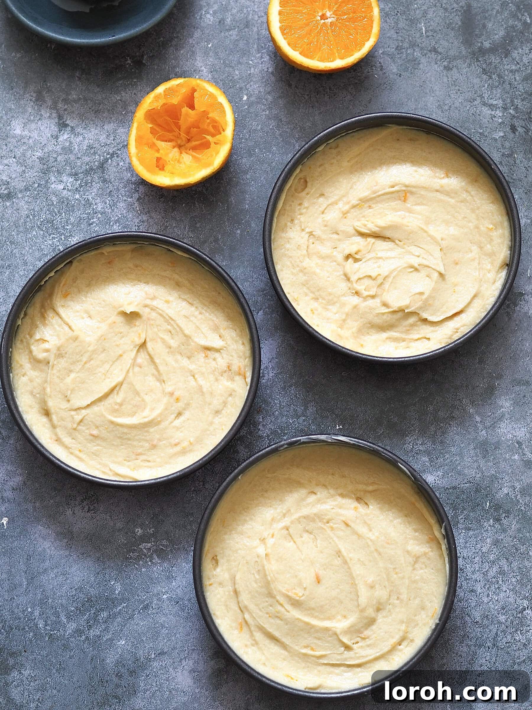 Three cake sponges in their tins, ready to be baked in the oven, with golden tops.