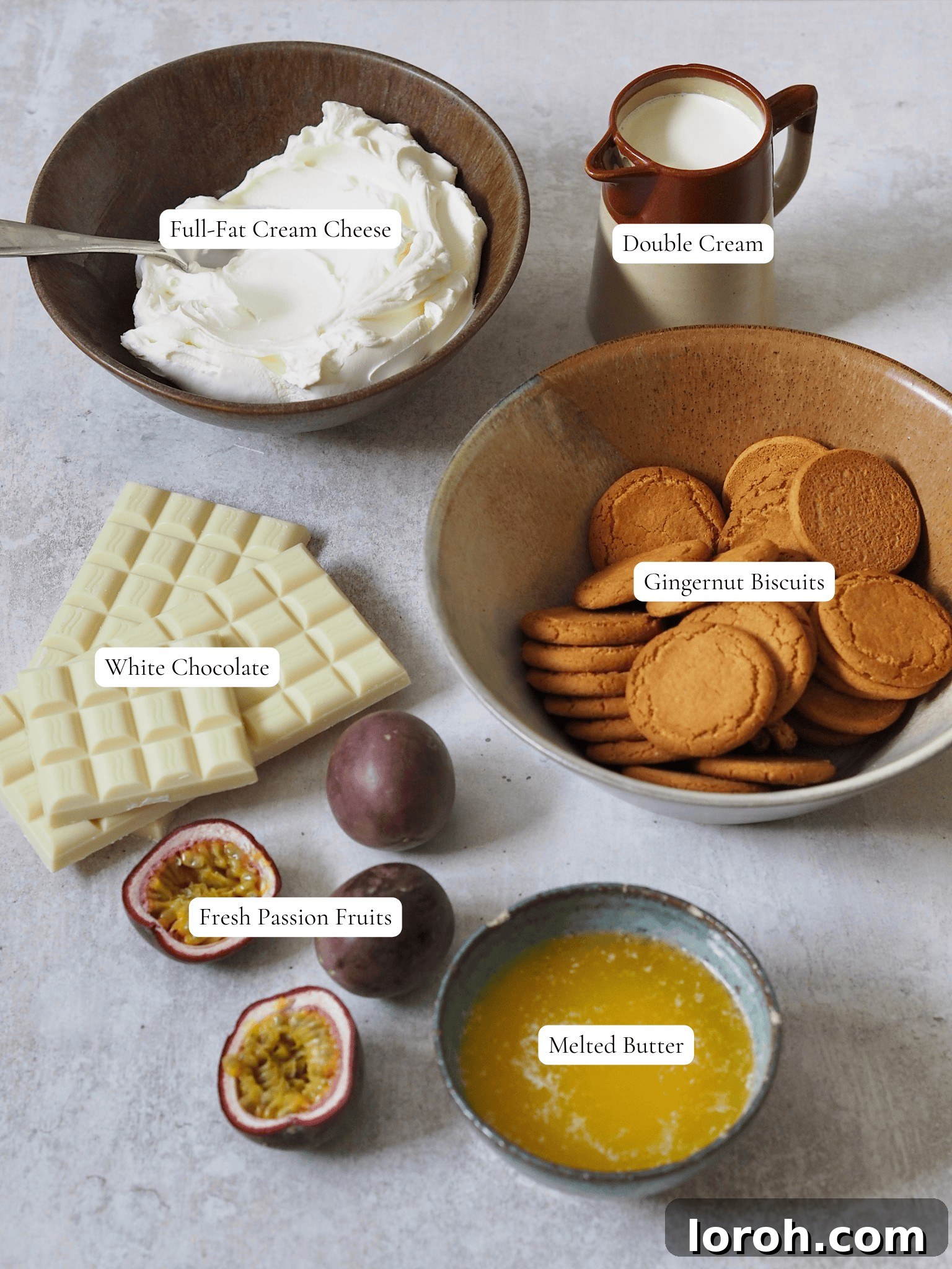 Neatly arranged ingredients for making white chocolate and passion fruit cheesecake, including biscuits, butter, white chocolate, cream cheese, double cream, and fresh passion fruits.