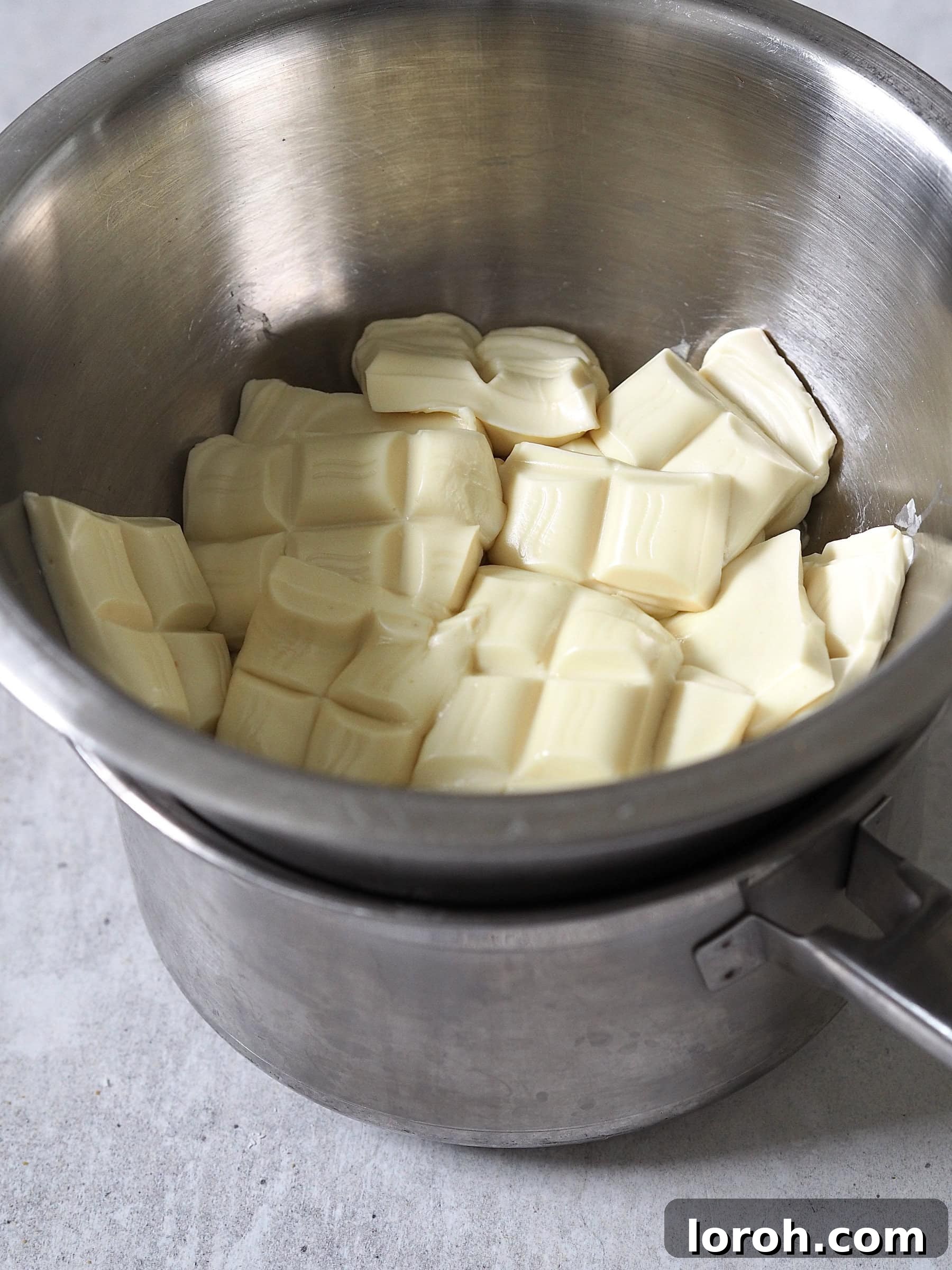 White chocolate pieces melting gently in a heatproof bowl set over simmering water, creating a smooth ganache.