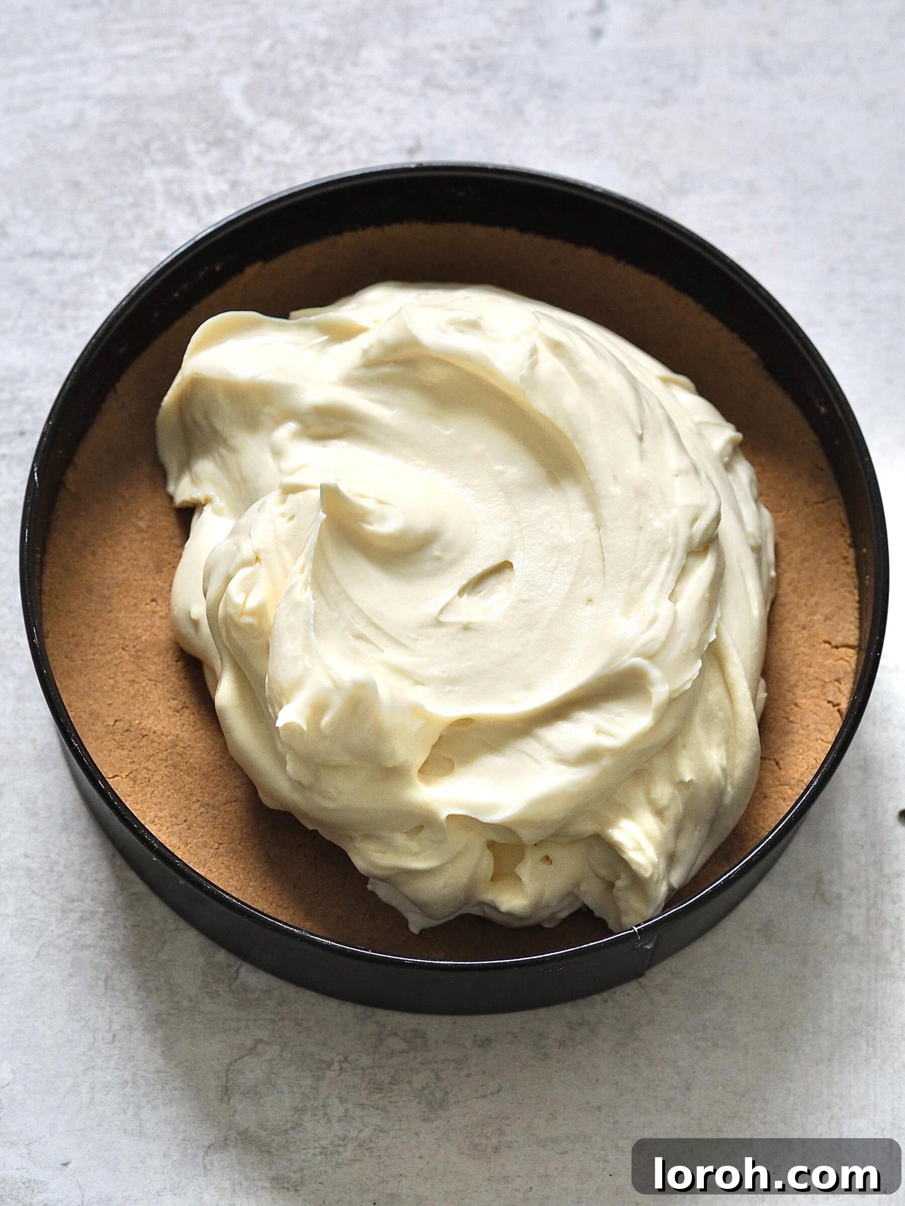 The passion fruit cream topping spread evenly over the biscuit base in the springform tin, ready for chilling.