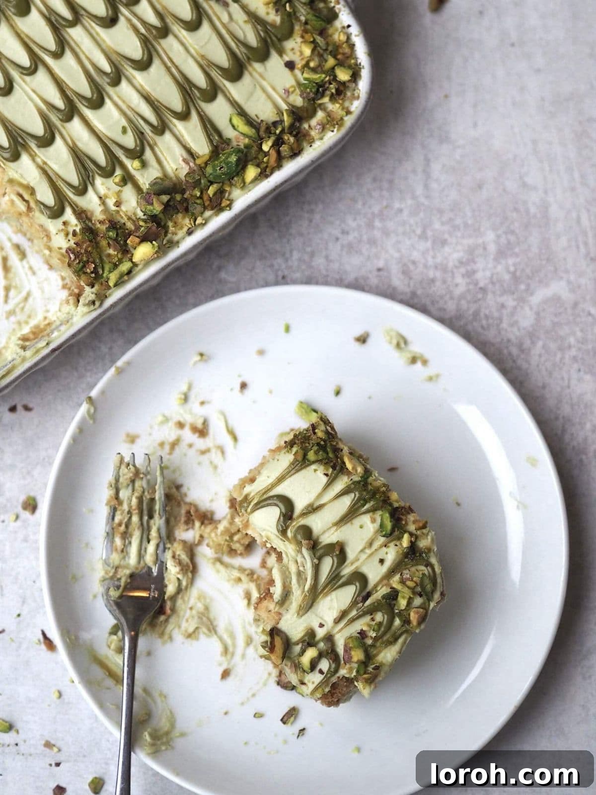 Pistachio Tiramisu in a white serving dish with a single slice on a plate, garnished with chopped pistachios.