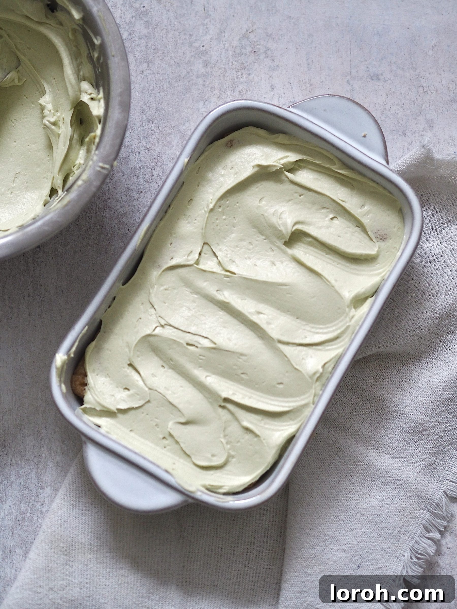 A layered Pistachio Tiramisu during assembly, showing cream over ladyfingers.