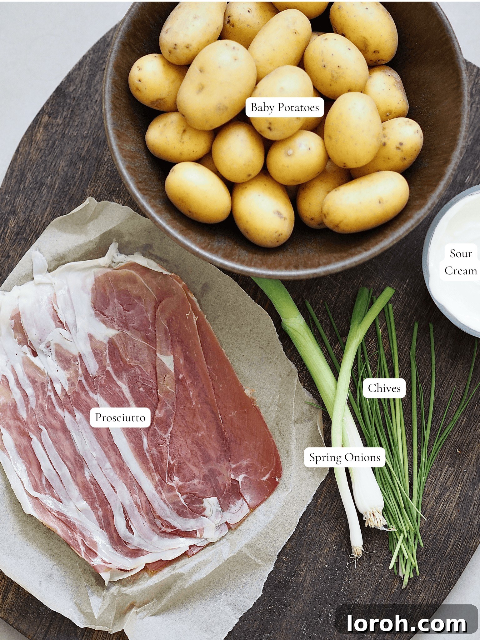 Air Fried Accordion Potatoes 4 Labeled ingredients for air fryer hasselback potatoes, including baby potatoes, oils, salt, prosciutto, spring onions, chives, sour cream, and chili flakes.
