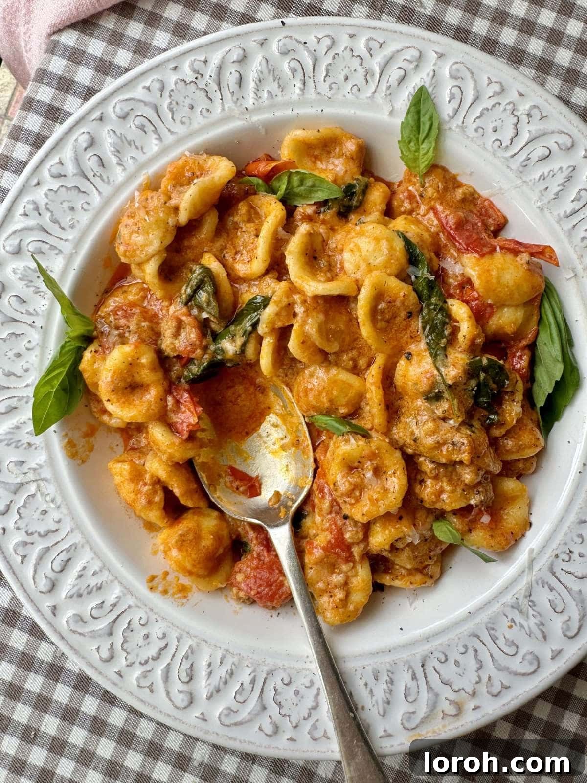 A close-up shot of creamy Sausage Nduja Pasta served in a white bowl, garnished with fresh basil and Parmesan cheese.