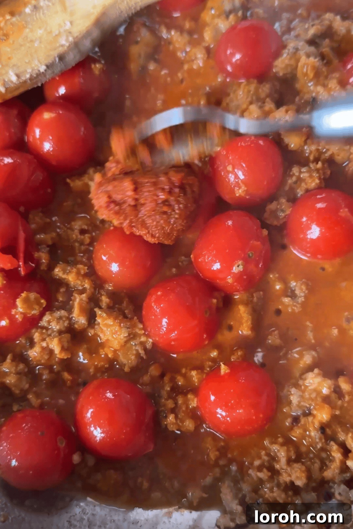 Cherry tomatoes, tomato paste, and Nduja paste being added to crispy sausage in a pan.