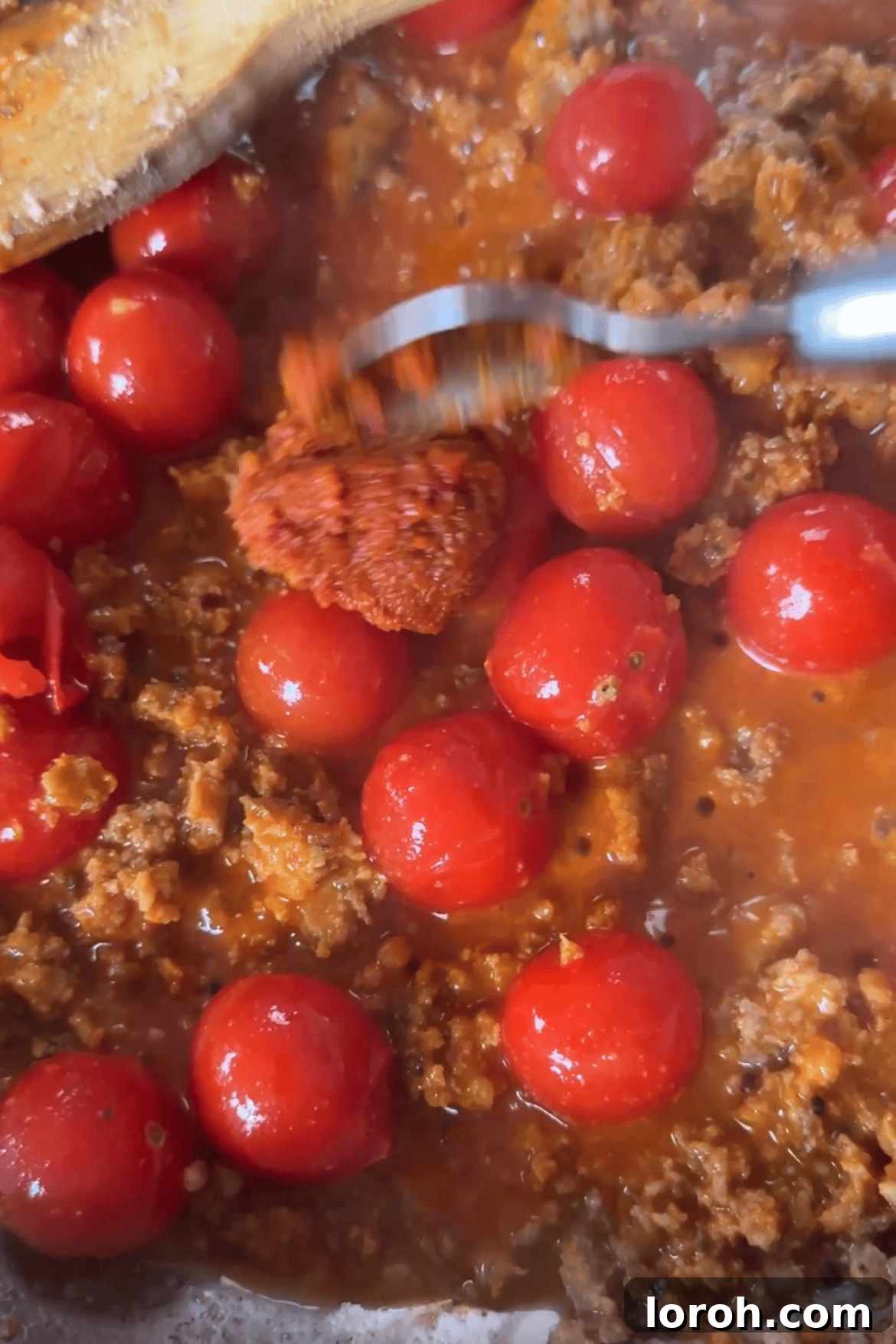 Adding cherry tomatoes, tomato puree, and nduja paste to the fried sausage in a pan.