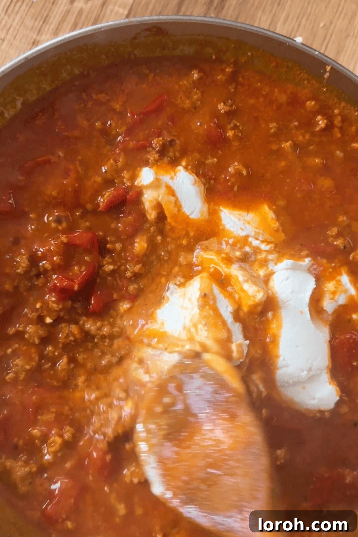 Adding mascarpone to the simmering tomato and sausage sauce in a pan.