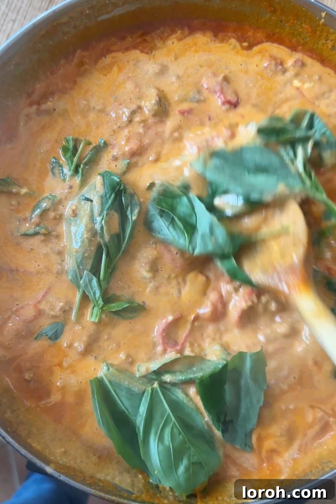 Stirring fresh basil leaves and a splash of pasta water into the creamy sausage and tomato sauce.