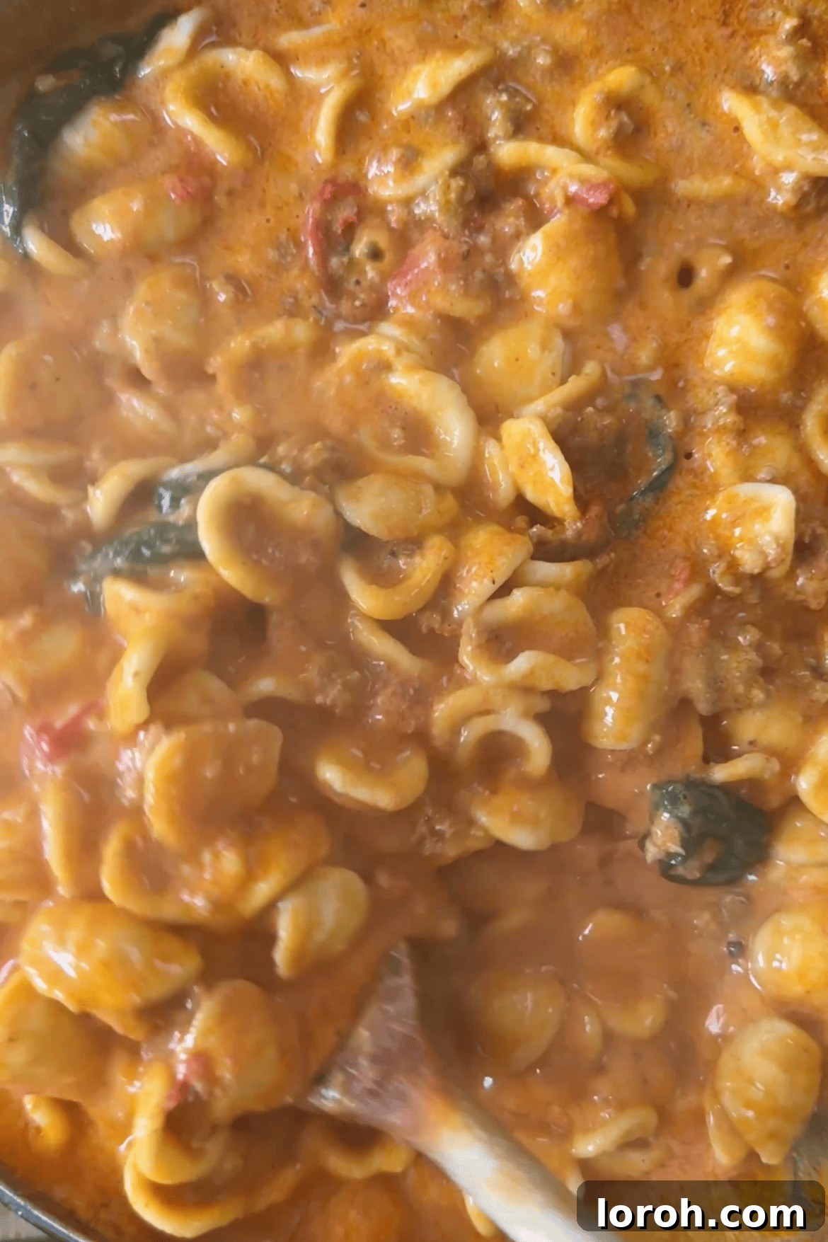 Mixing al dente cooked pasta with the creamy sausage and tomato sauce, parmesan, and fresh basil.