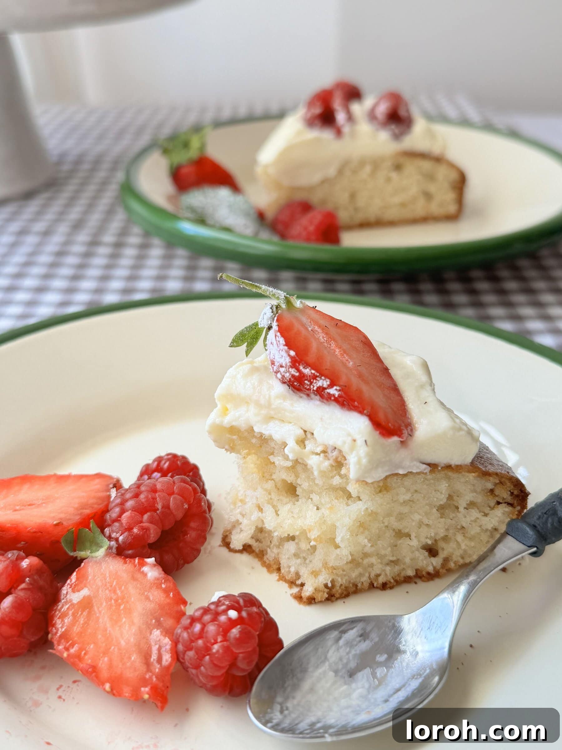 French Yogurt Cake The Easiest No Measure Treat 3 A slice of Gâteau au Yaourt on a white plate, adorned with fresh strawberries and a dusting of icing sugar.