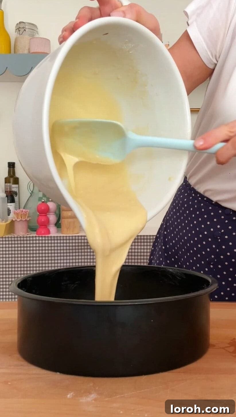 French Yogurt Cake The Easiest No Measure Treat 6 The smooth cake batter being poured from the mixing bowl into a prepared round cake tin.