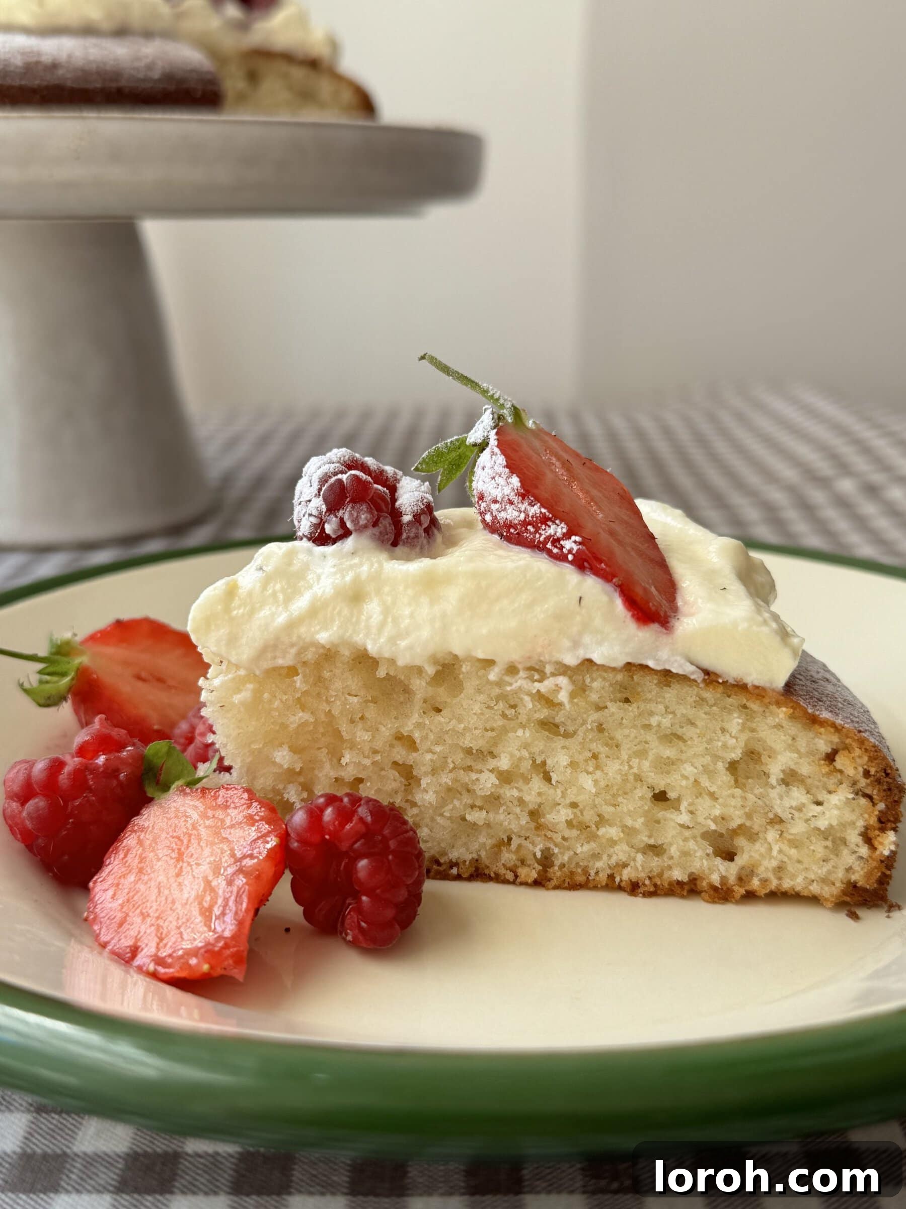 French Yogurt Cake The Easiest No Measure Treat 8 A close-up of a Gâteau au Yaourt slice, showing its moist, tender crumb, topped with fresh raspberries on a white plate.