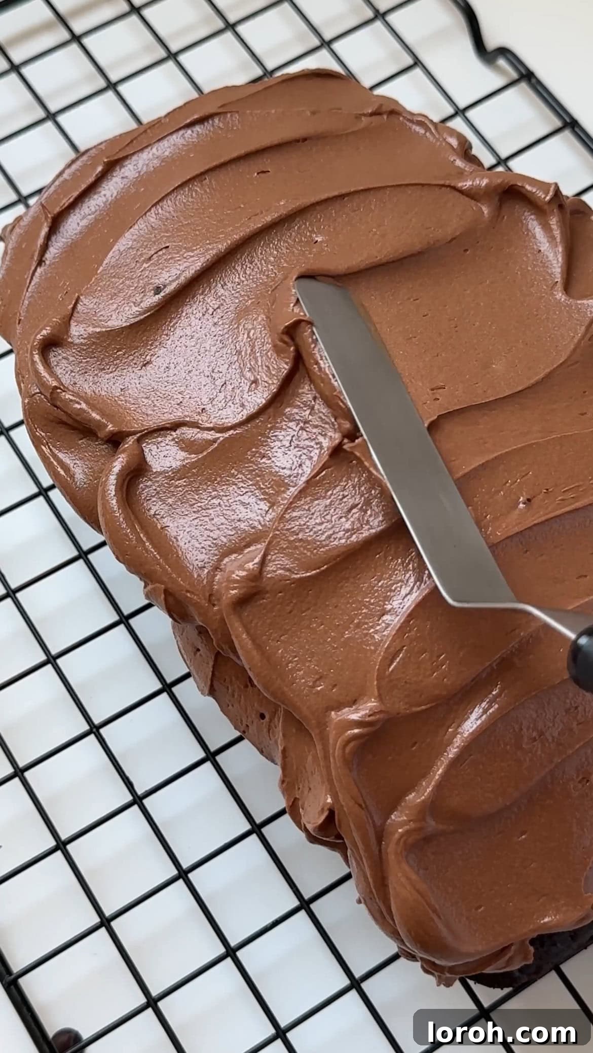 Fudgy Chocolate Zucchini Cake 10 A palette knife spreading smooth, dark chocolate frosting over the top of a cooled chocolate courgette loaf cake.