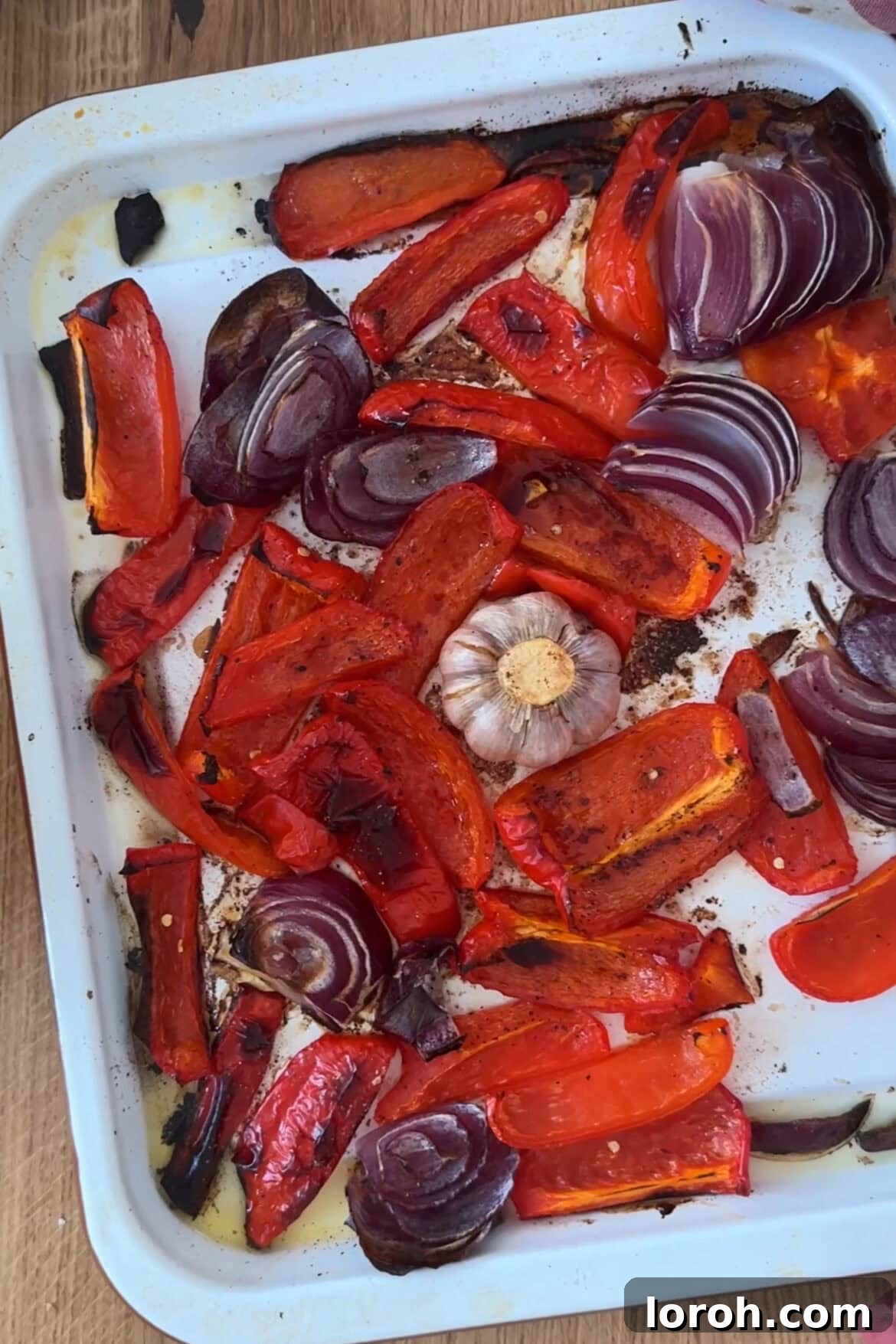 Velvety Roasted Red Pepper Sauce 3 Close-up of freshly roasted red bell peppers, onions, and garlic on a baking sheet, glistening with oil.