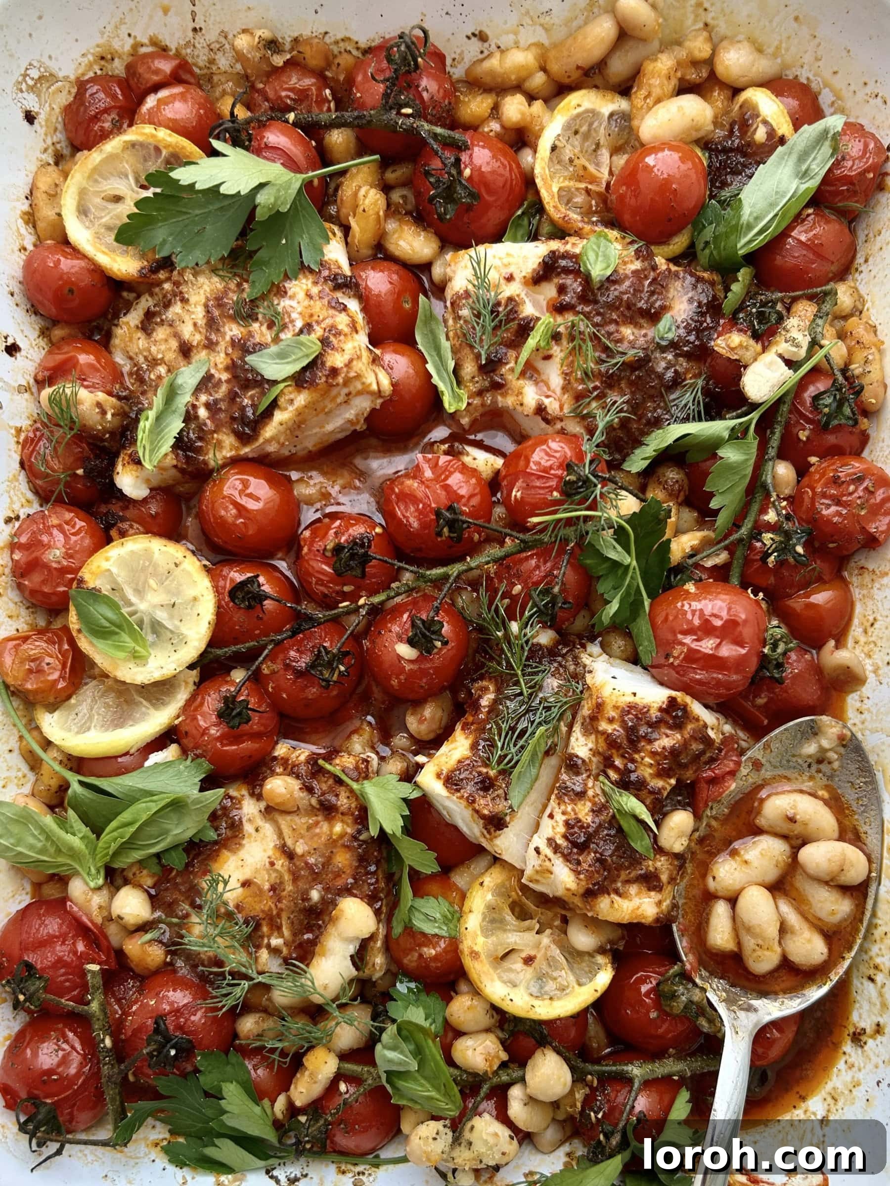 Spooning tender white beans from a harissa cod and cherry tomato traybake, ready to serve.