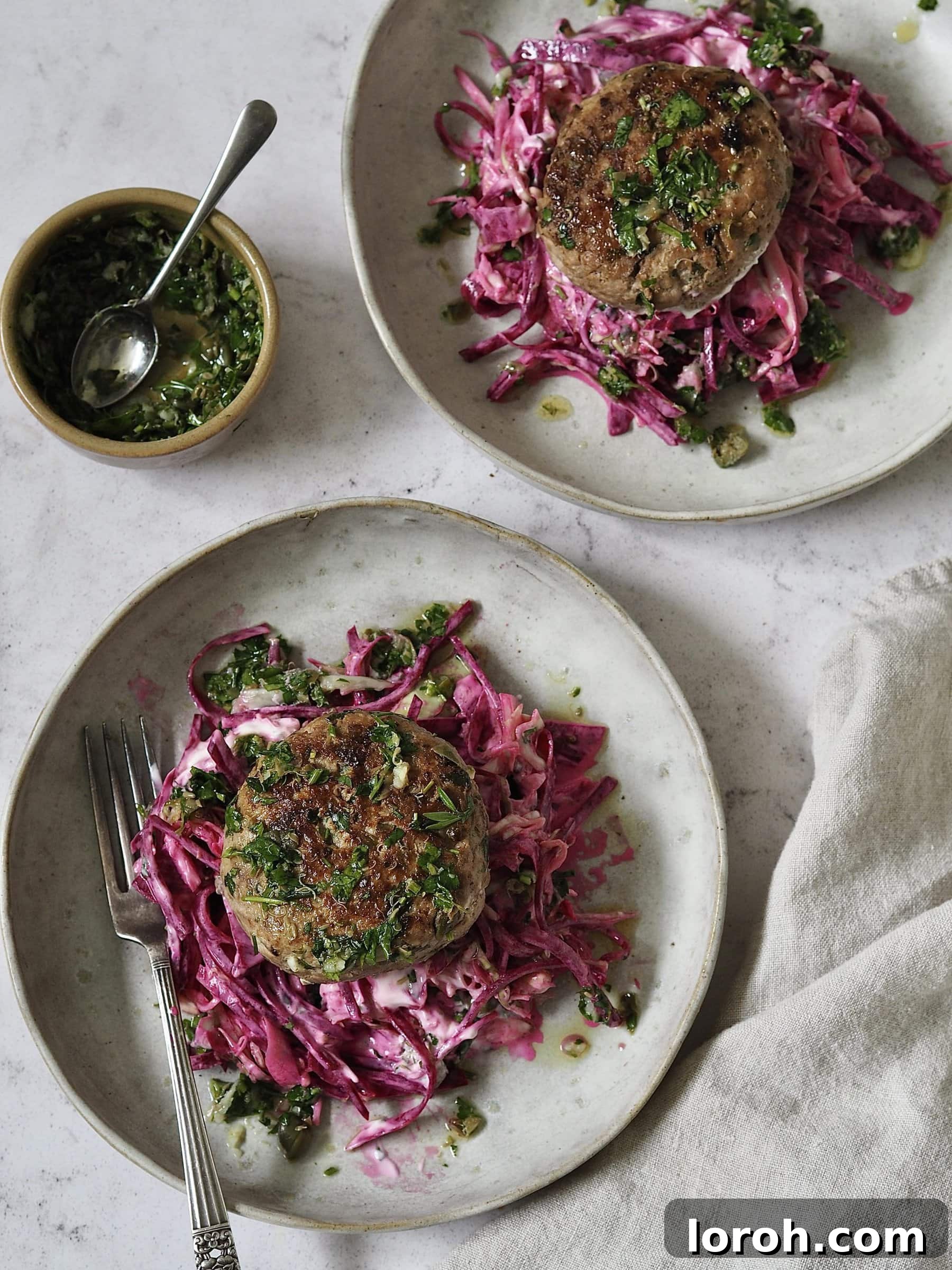 Chicken burgers served on generous piles of pink yogurt and beetroot slaw on grey stone plates, with extra salsa verde spooned over the top.