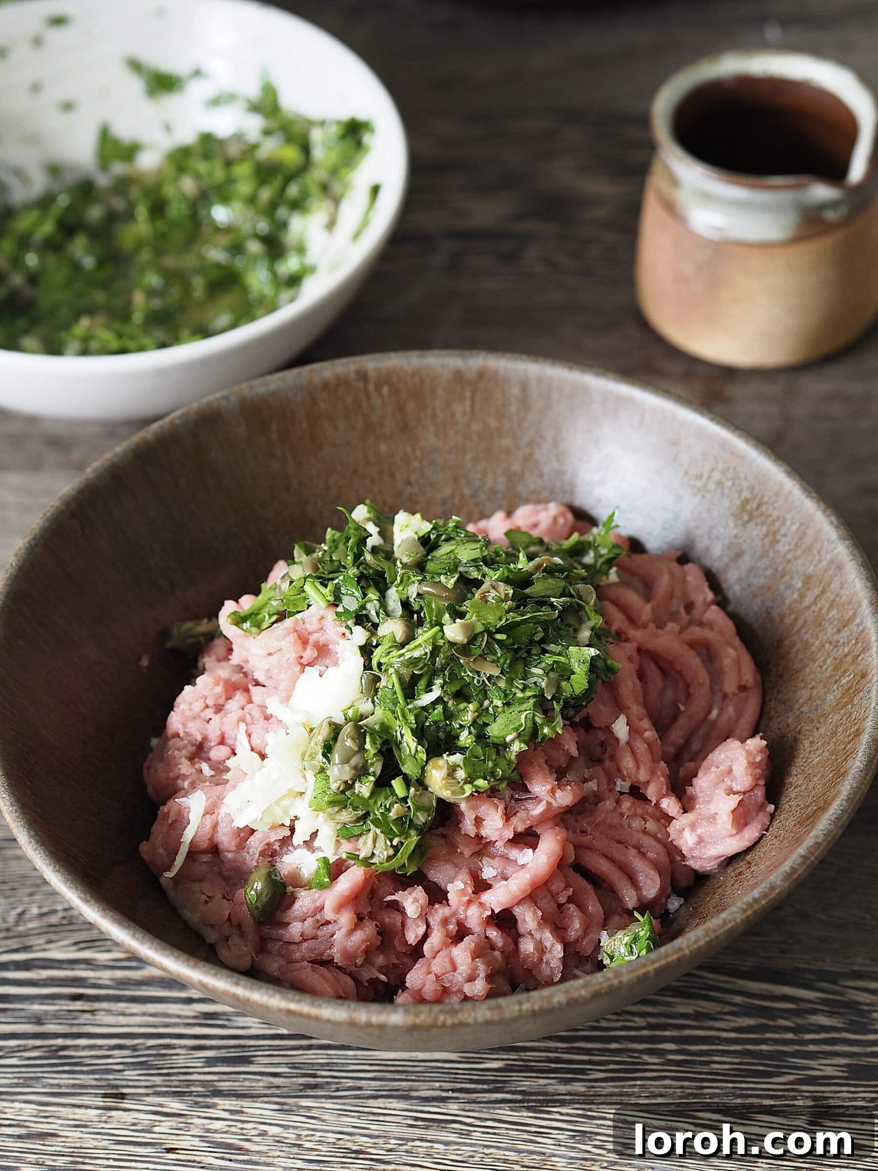 Raw chicken mince in a bowl, topped with a dollop of vibrant green salsa verde, ready to be mixed.
