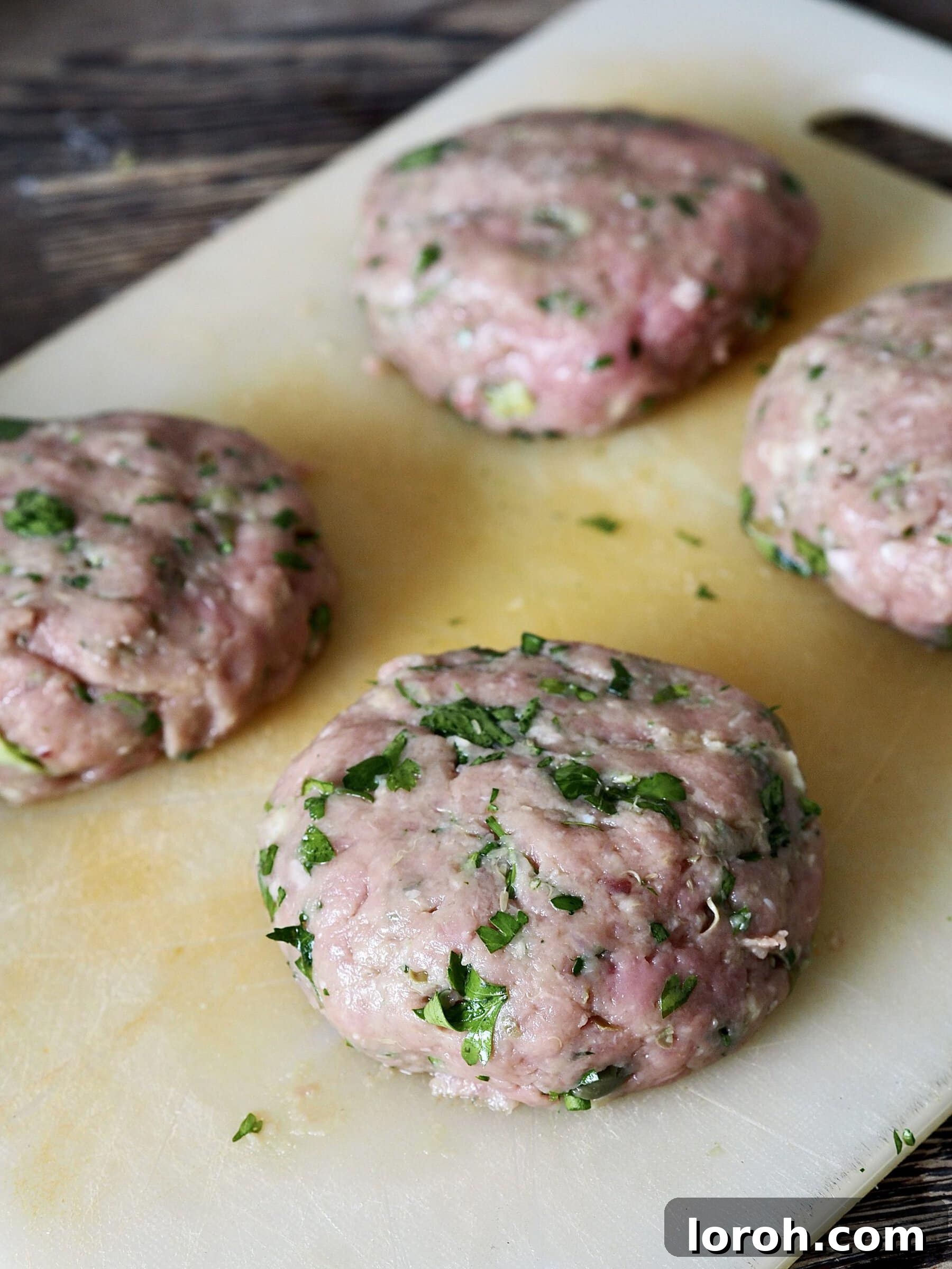 Four perfectly shaped raw salsa verde chicken burgers on a white cutting board, ready for chilling and cooking.