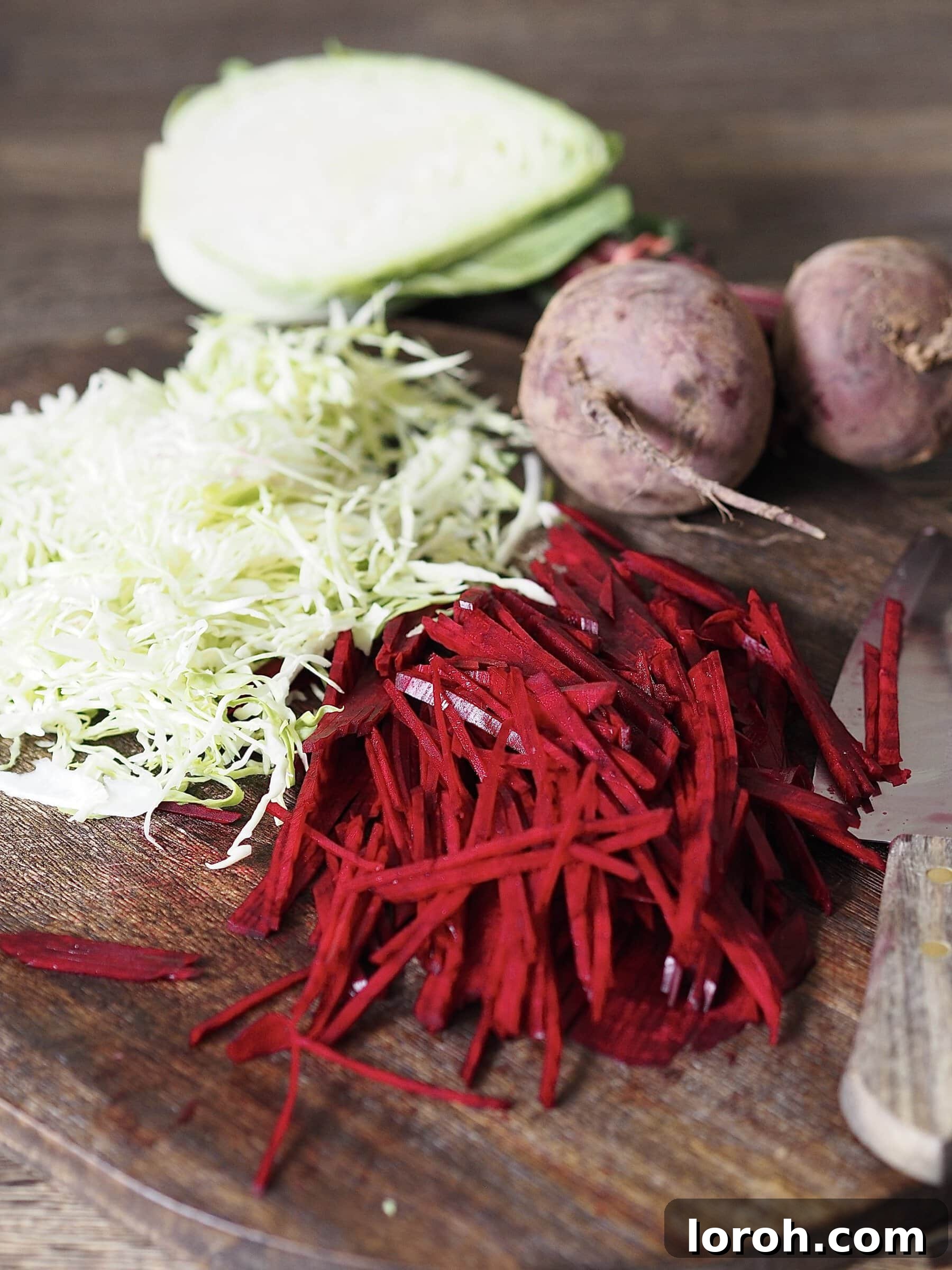 Finely sliced sweetheart cabbage and raw beetroot on a wooden cutting board, prepared for the vibrant slaw.