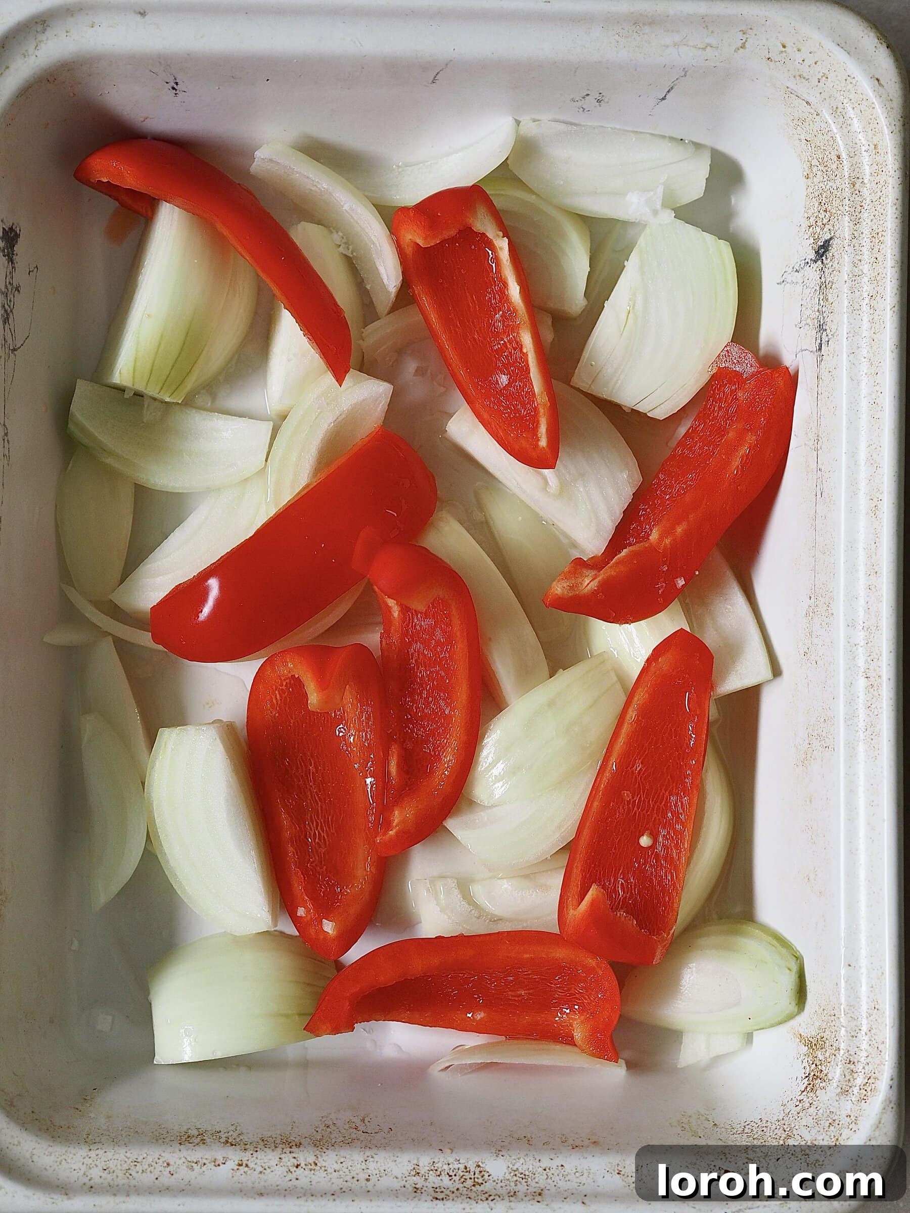 Zesty Peri Peri Chicken with Golden Potato Wedges 5 Chopped white onions and red peppers in a white roasting tray.