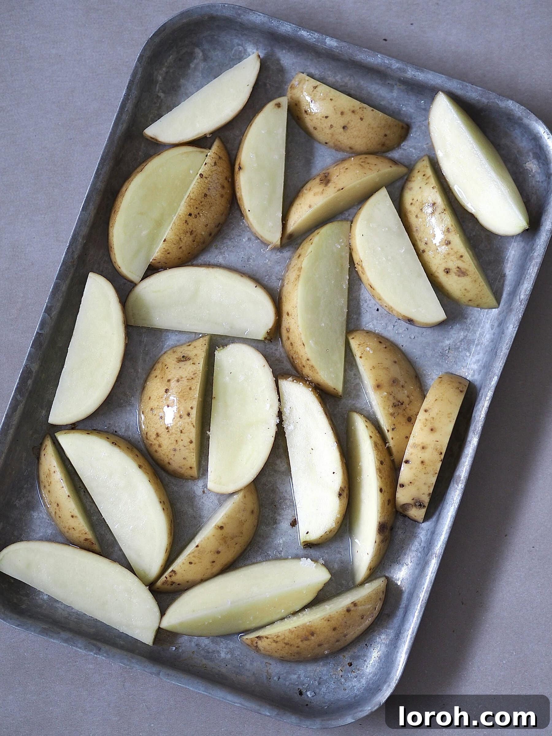 Zesty Peri Peri Chicken with Golden Potato Wedges 7 Raw potato wedges on a dark metal baking tray.