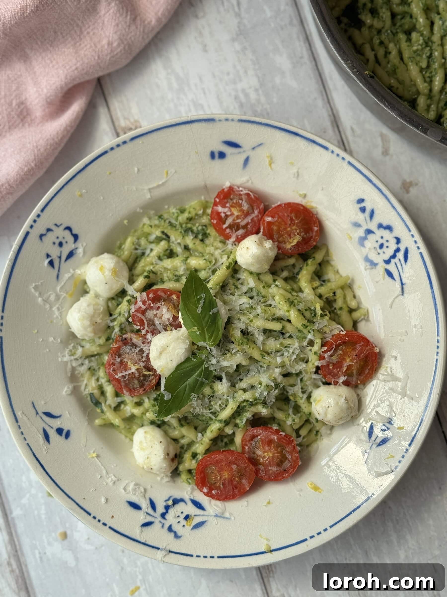 A beautifully plated bowl of Pasta al Pesto with fresh basil, mozzarella, and cherry tomatoes.