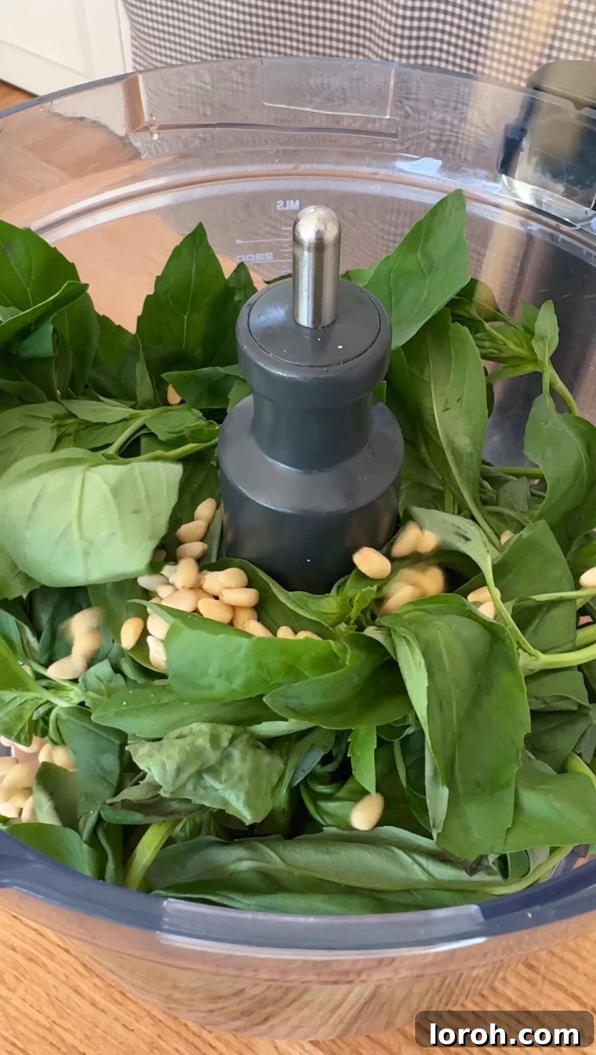 Adding fresh basil and toasted pine nuts to a food processor for pesto.