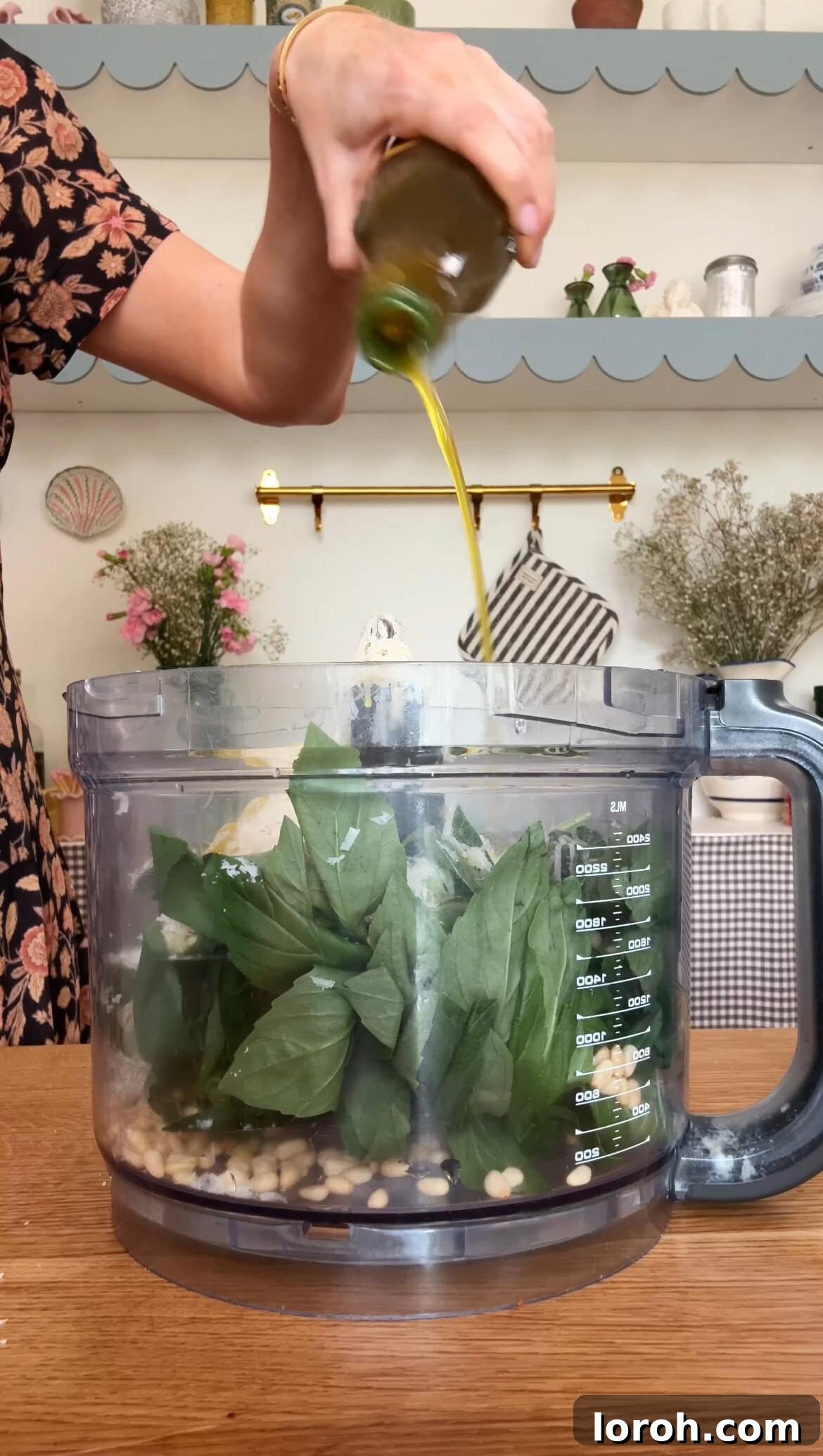 Pouring olive oil into the food processor with other pesto ingredients.