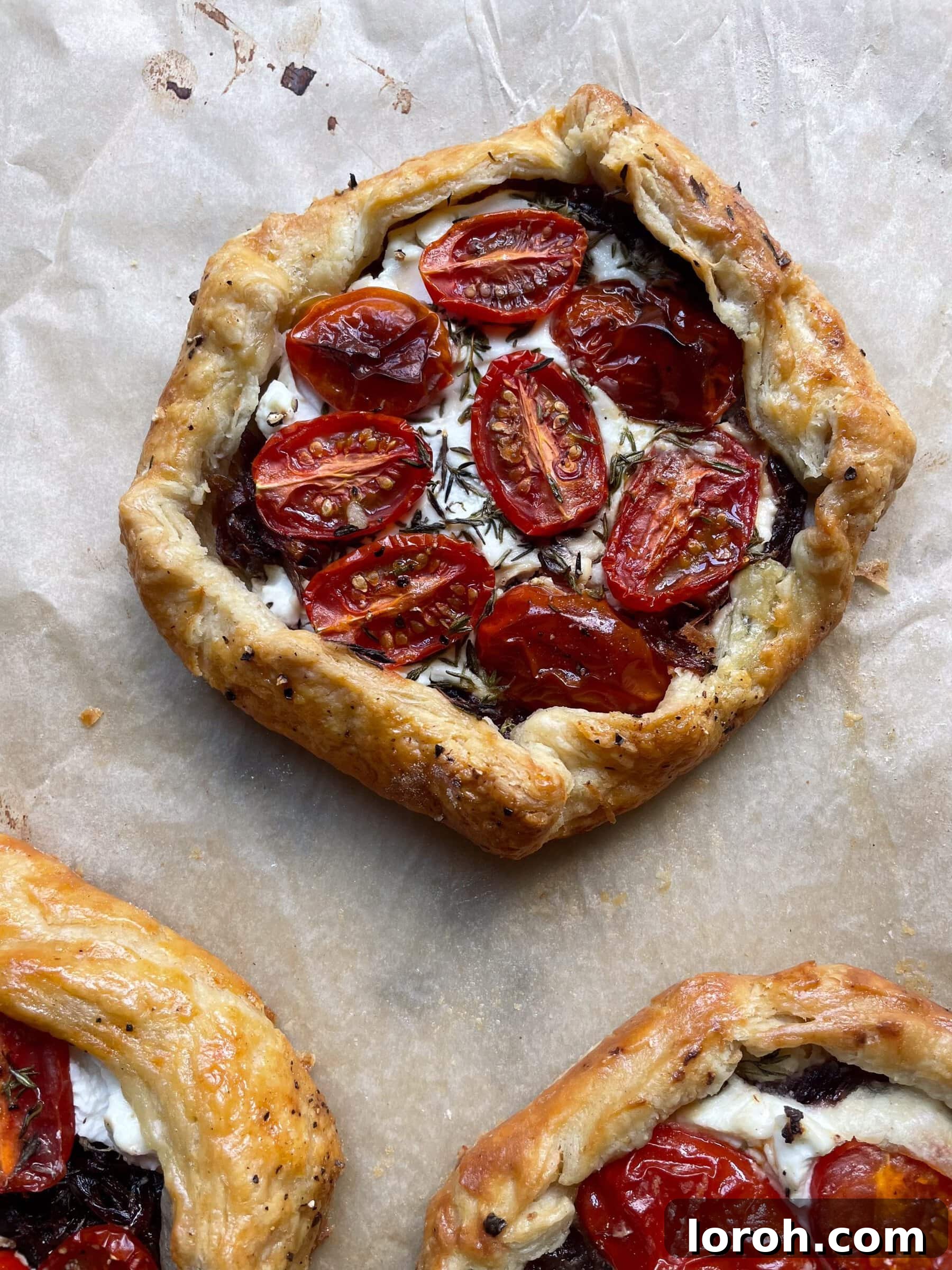 Sweet Onion and Goat Cheese Galettes with Sun-Kissed Cherry Tomatoes 3 Close-up view of a freshly baked caramelised onion galette on a parchment-lined baking sheet, showcasing its golden crust and delicious filling, ready to be served.