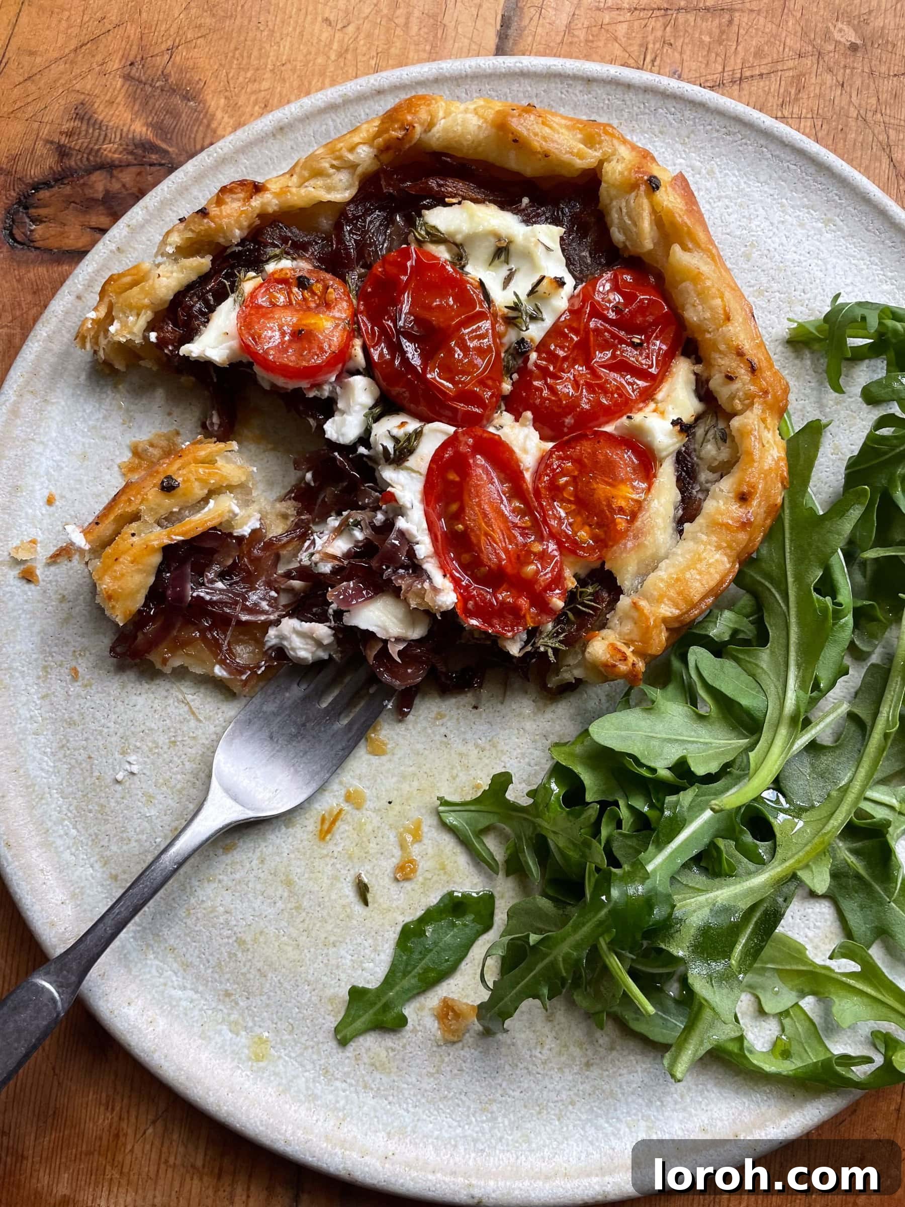 Sweet Onion and Goat Cheese Galettes with Sun-Kissed Cherry Tomatoes 6 A fork gracefully cutting into a warm, inviting caramelised onion, cherry tomato, and goat cheese galette, revealing its tender filling and flaky crust.