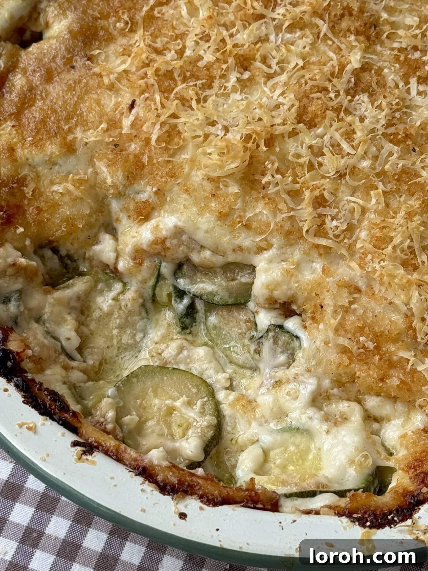 A close-up of a bubbling Gratin de Courgettes in a baking dish, highlighting the rich, creamy texture of the sauce and the beautifully golden, crisp cheese topping.