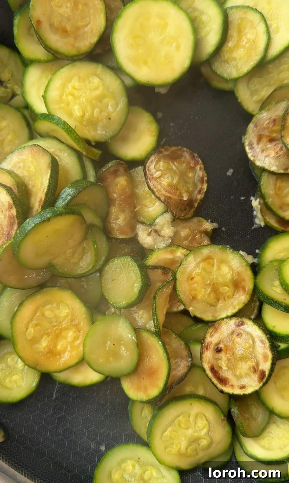 Adding minced garlic to the softened courgettes in a pan, infusing them with aromatic flavor before transferring to a baking dish.