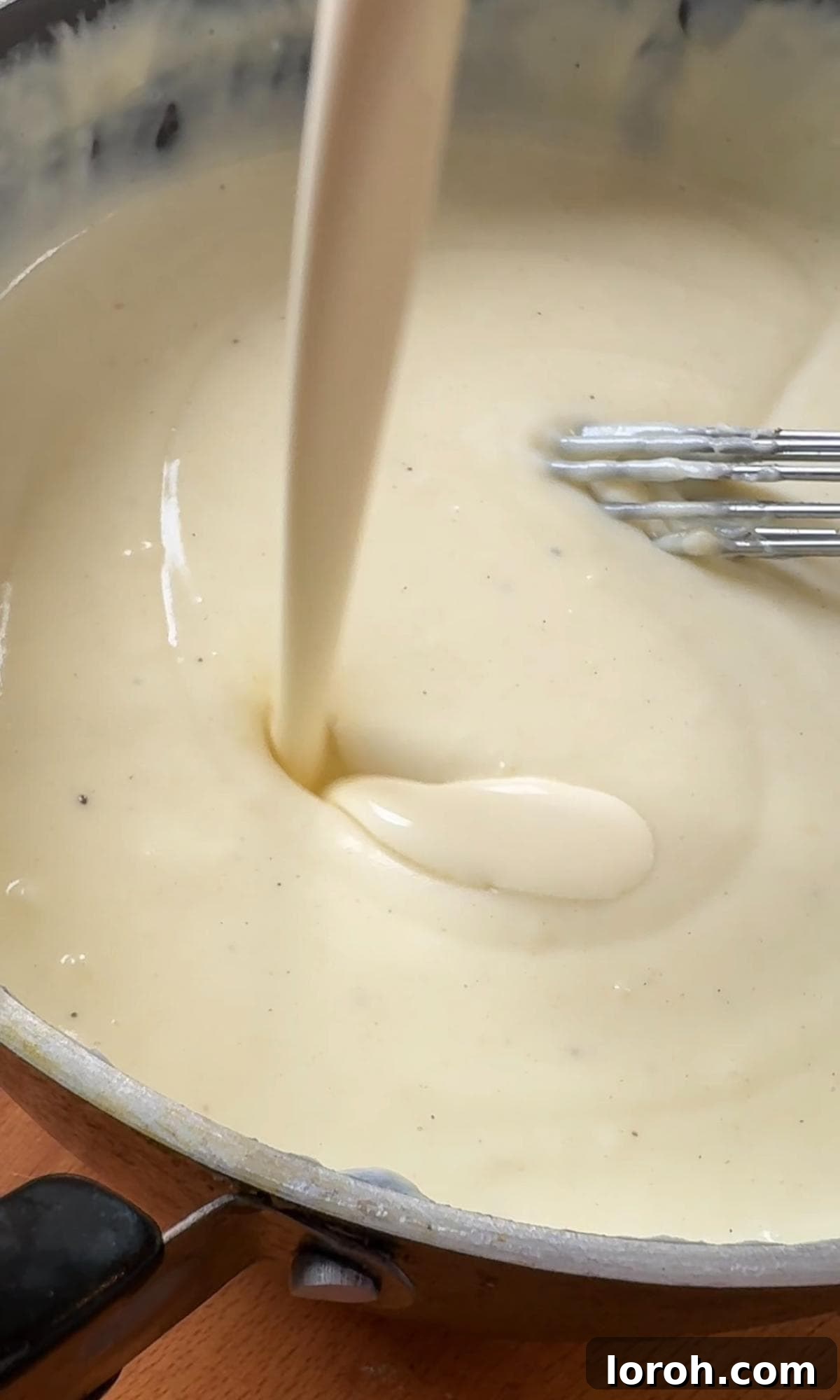 Adding a generous amount of grated cheese and double cream to the thickened béchamel sauce, stirring to combine for the gratin.