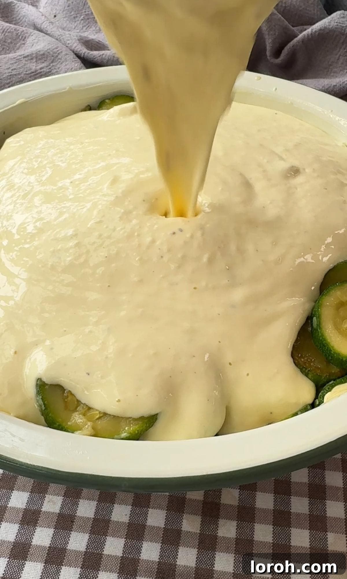 Carefully pouring the creamy cheese sauce evenly over the sautéed courgettes spread out in the ovenproof baking dish.