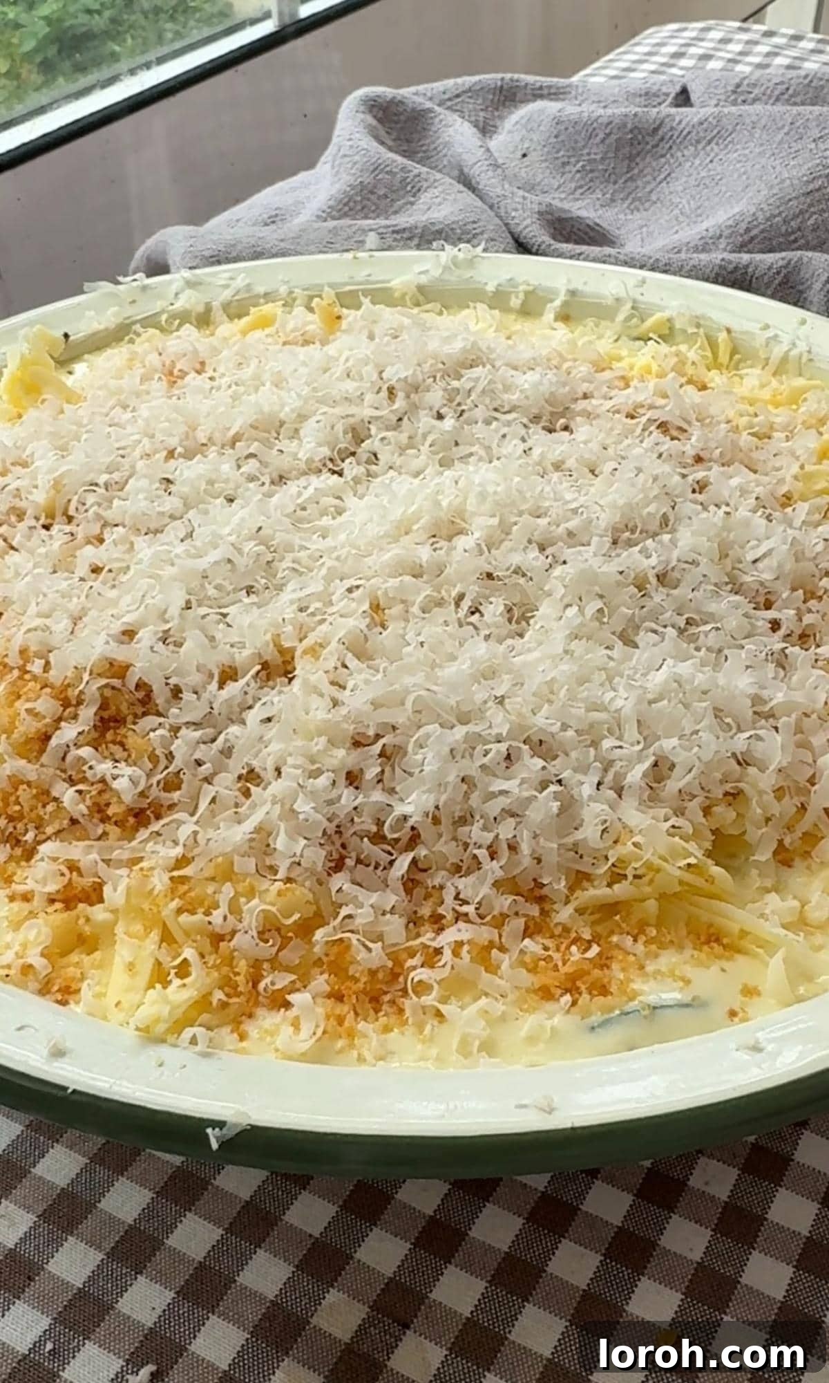 Sprinkling the reserved grated cheese and breadcrumbs over the gratin for a crispy, golden crust before it goes into the oven.