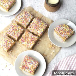 Individual white plates presenting perfectly cut squares of iced sprinkle sponge cake, with the remaining cake still in the tin in the background, ready for serving.