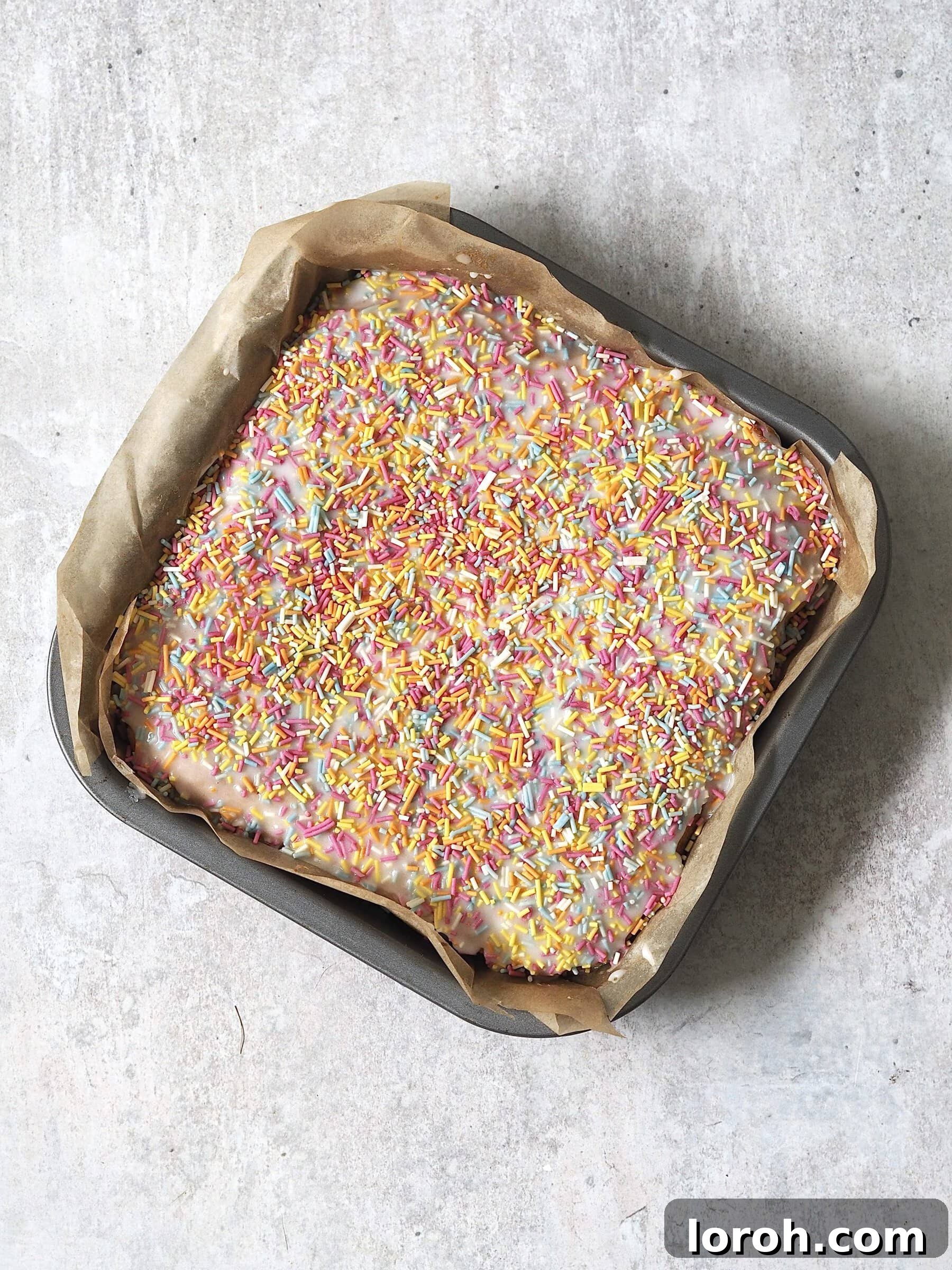 Classic Sprinkle Sponge with Golden Custard 9 A beautifully iced and sprinkle-decorated school sponge cake still in its lined tin, ready to be cut and served.