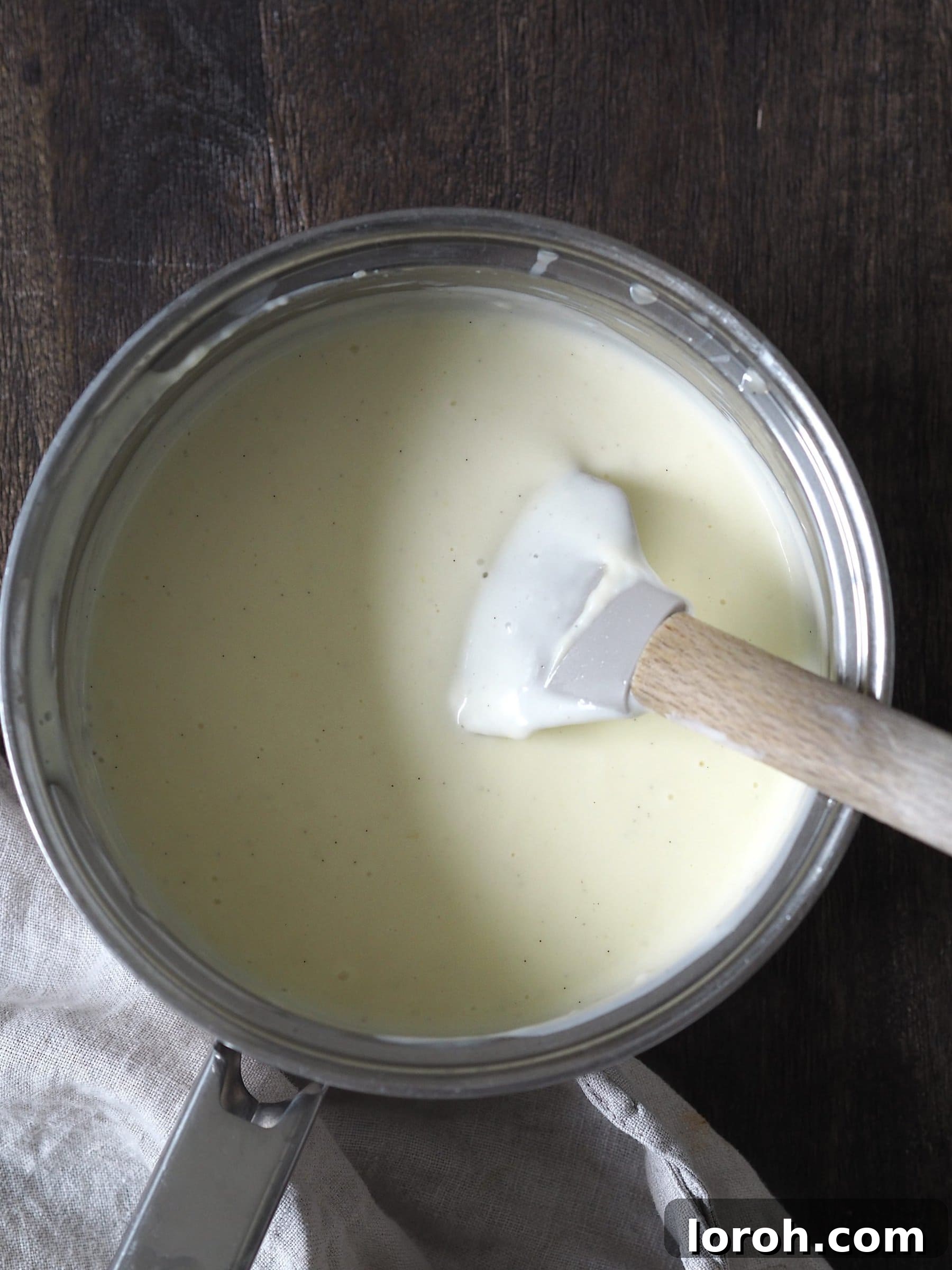 Classic Sprinkle Sponge with Golden Custard 10 A rubber spatula diligently stirring a rich, creamy saucepan of homemade custard, ensuring a smooth and lump-free texture.